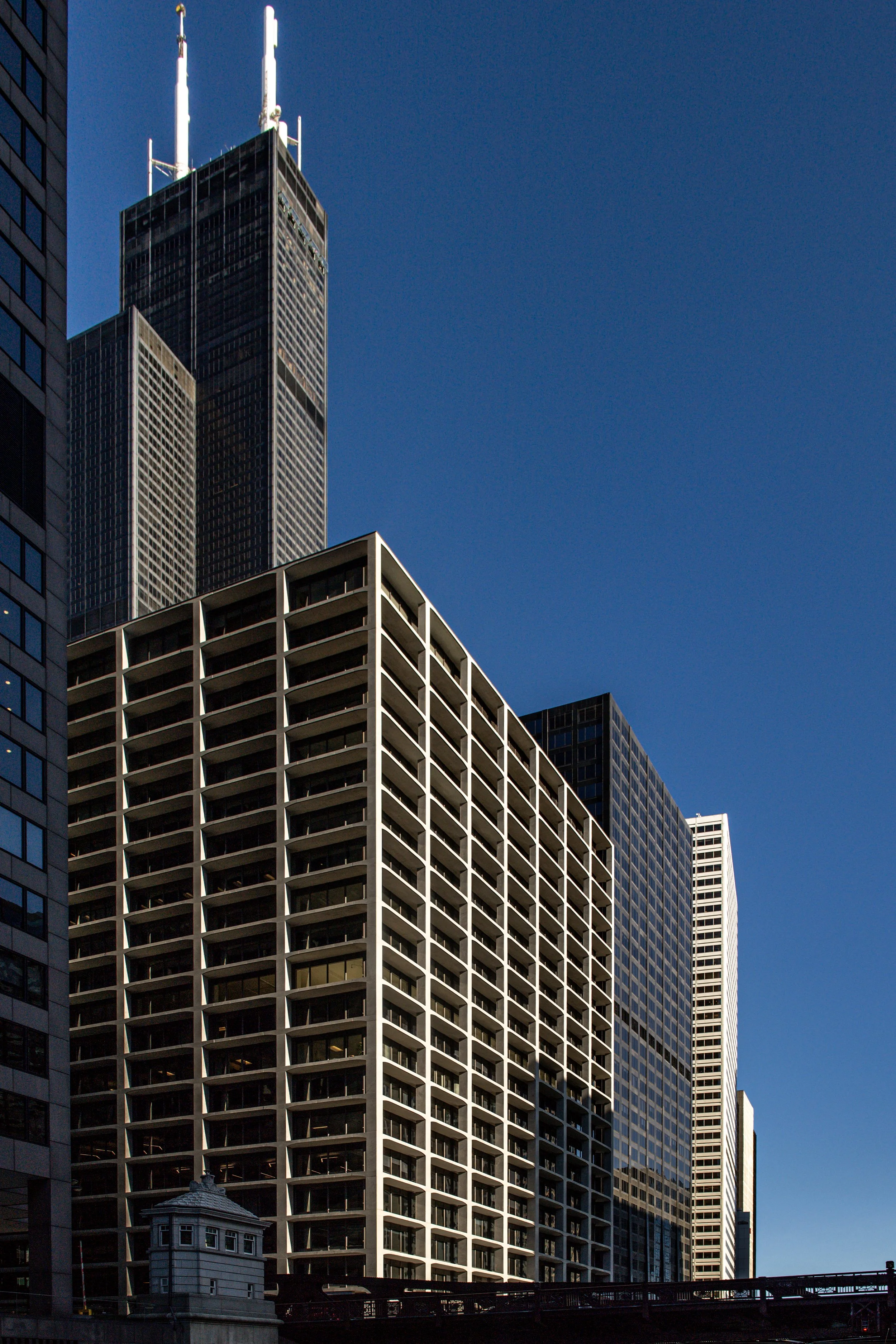 High-rise city buildings against a clear blue sky, including a skyscraper with antennas on top.