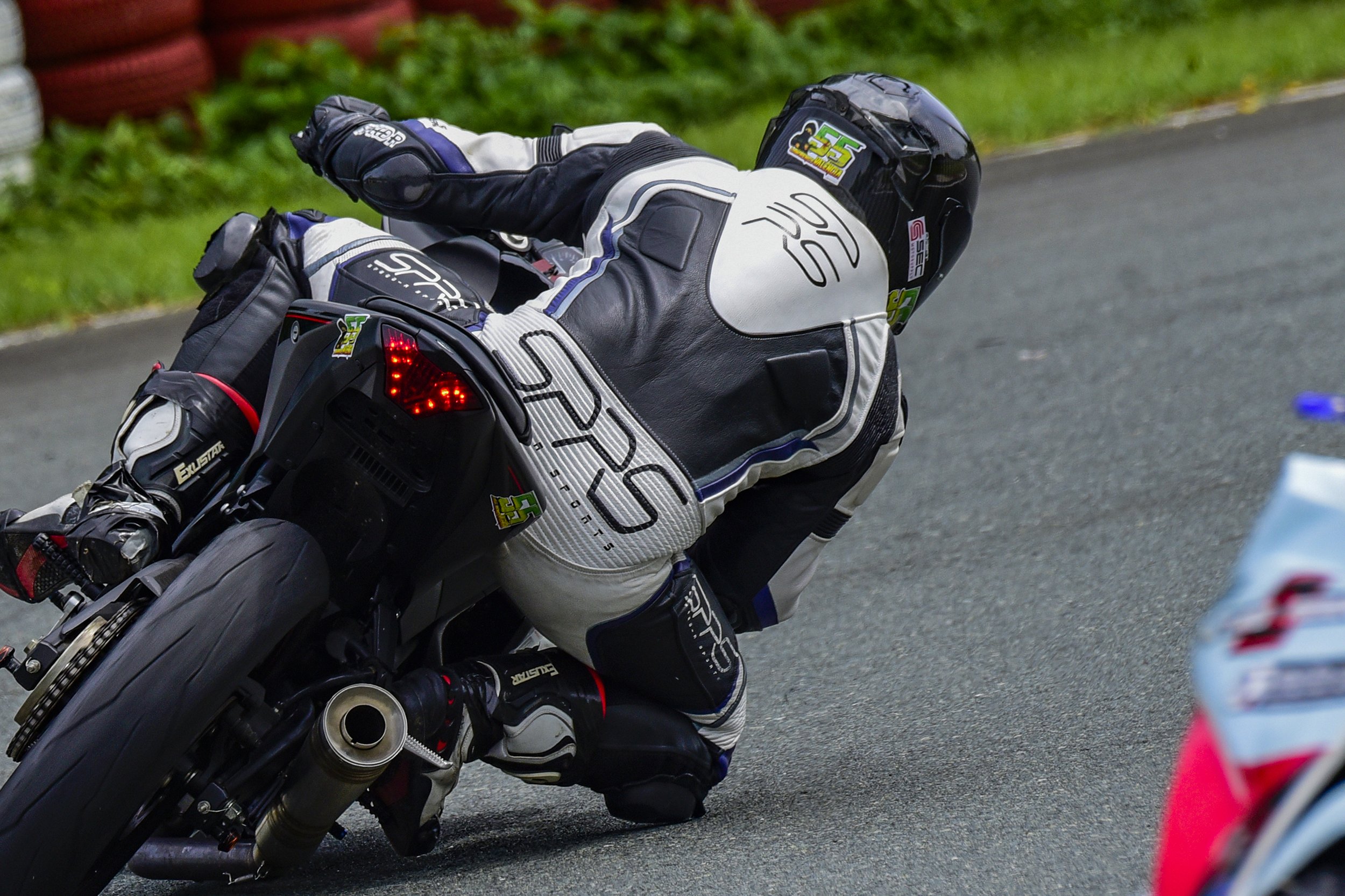Motorsport rider leaning into a turn on a race track, wearing full protective gear and a black helmet, motorcycle with racing decals, on an asphalt track with grassy area in the background. rider Lawrence Valencia