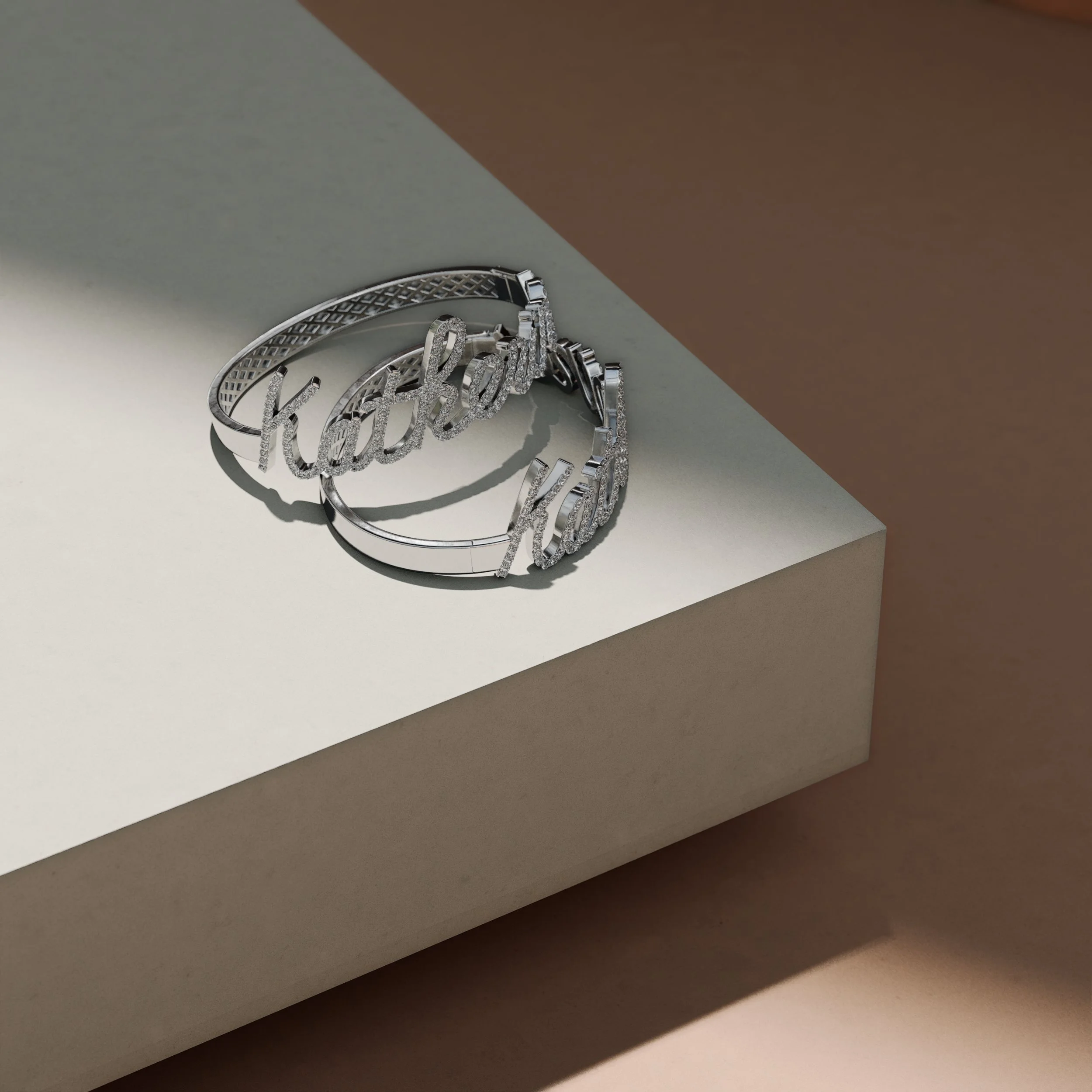 Silver jewelry with the word 'baby' written in cursive, placed on a white pedestal with a brown background.