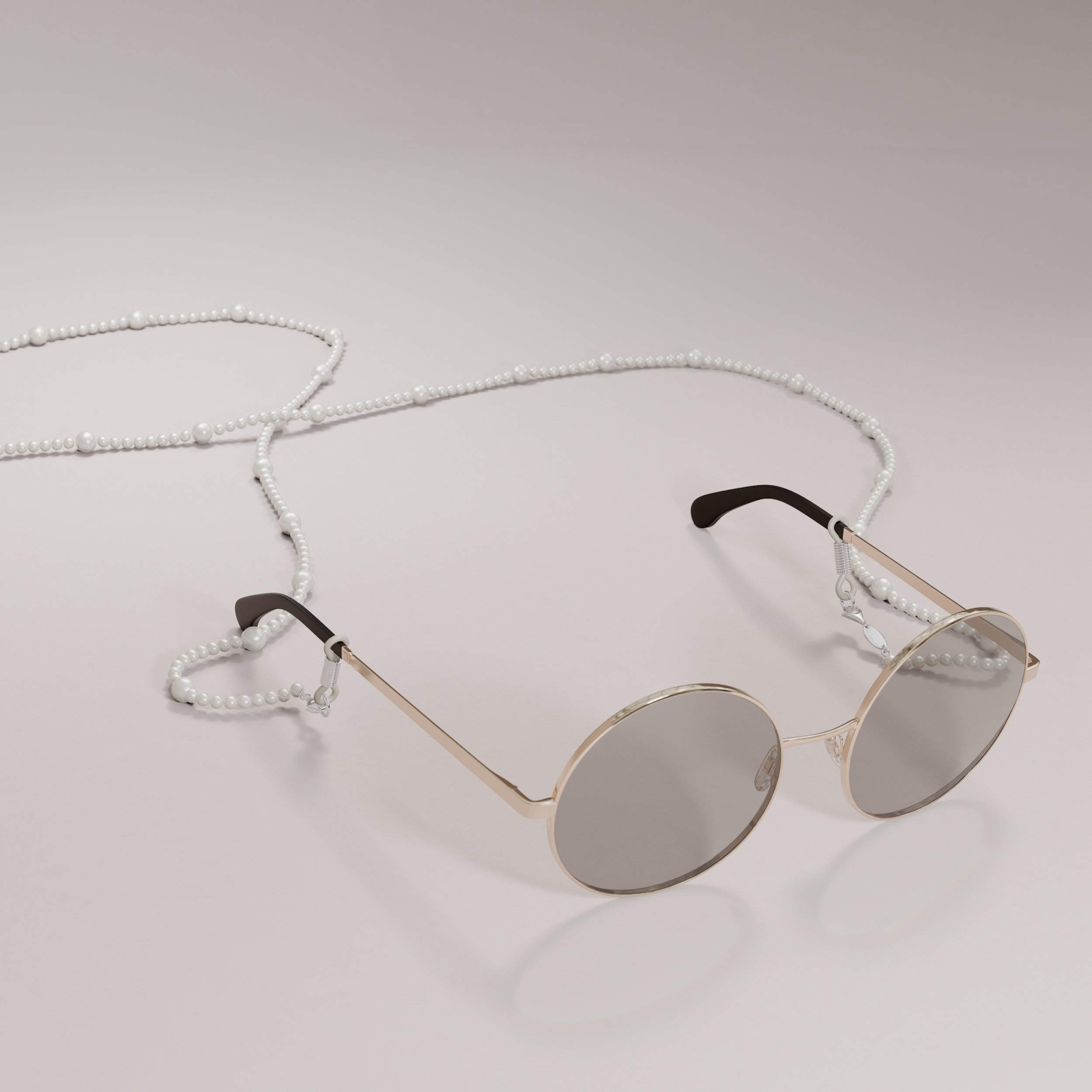 A pair of round sunglasses with gold frames and dark lenses resting on a white surface, attached to a pearl chain.
