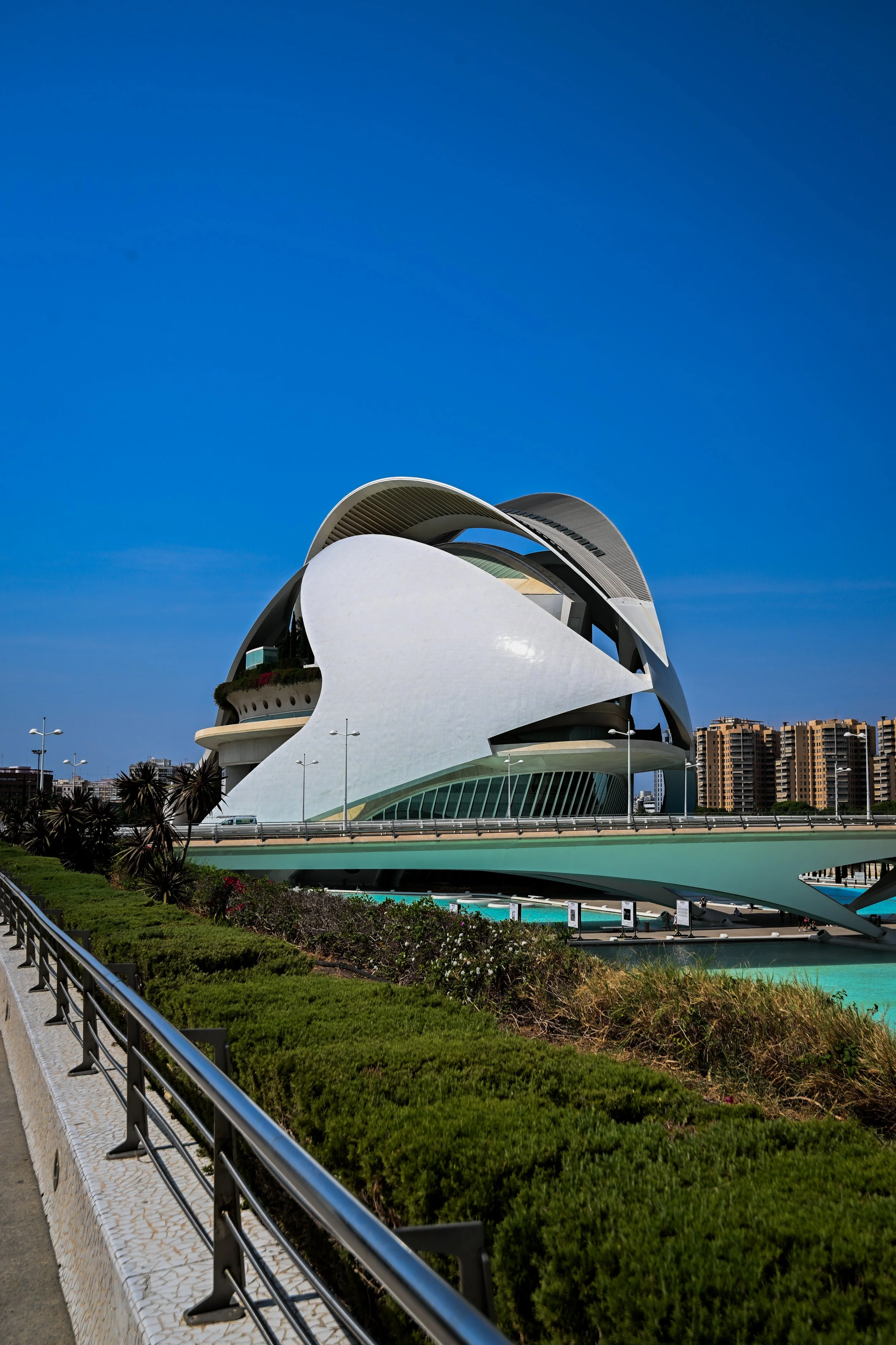 Modern, futuristic building with white and black curved architecture under a clear blue sky, with greenery and a walkway in the foreground.