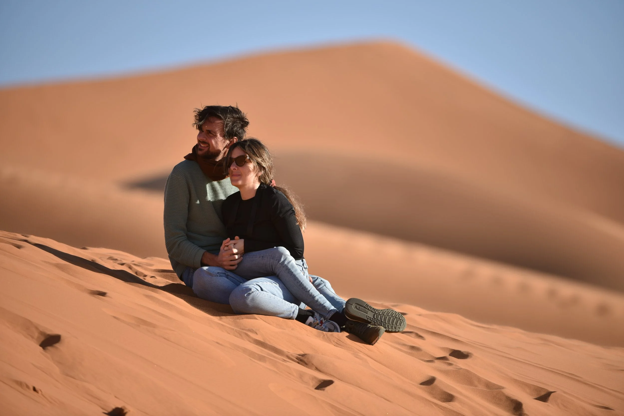 A couple sitting on sand dunes in a desert, enjoying the sunny day.