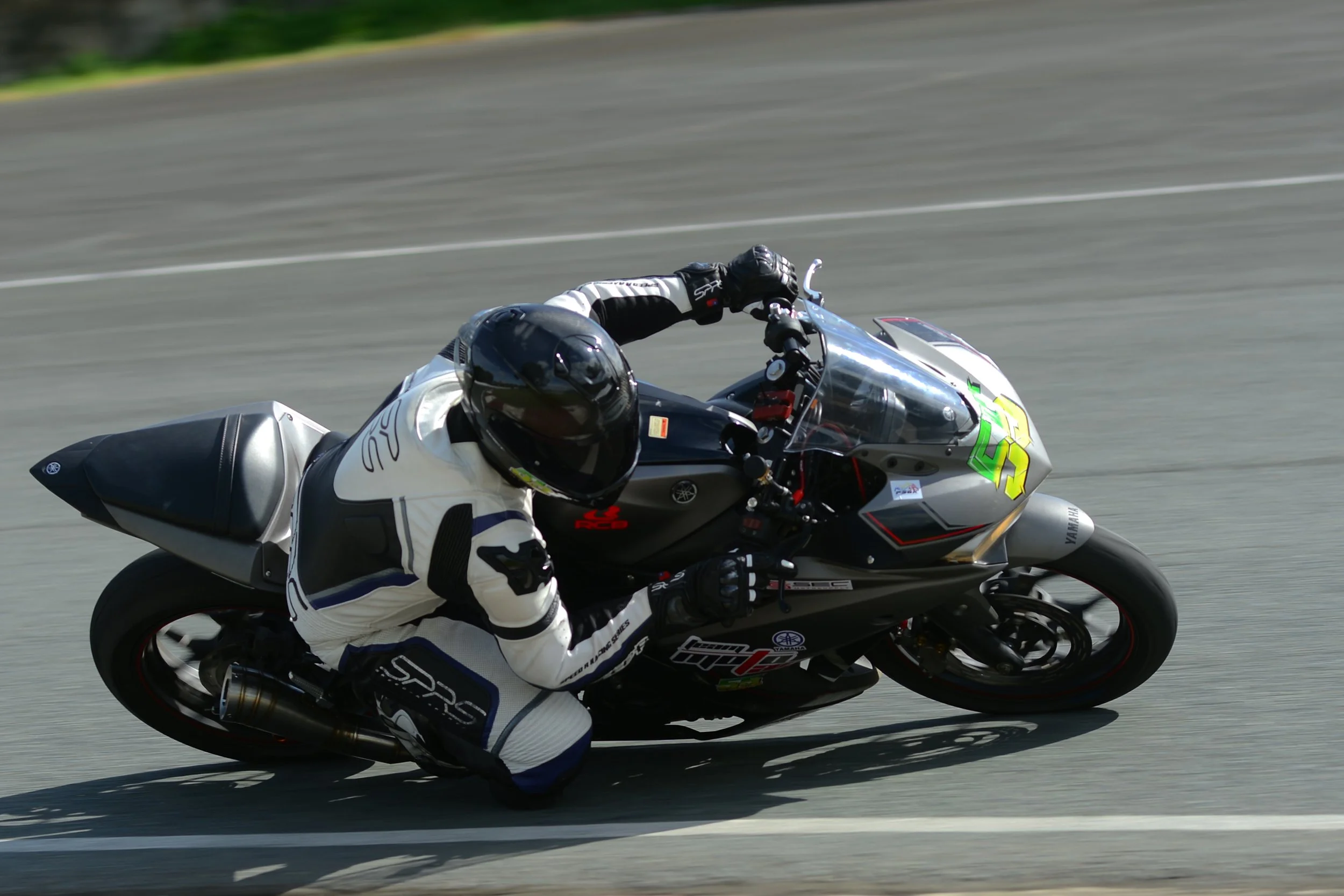 A motorcycle racer leaning into a turn on a race track, wearing a black helmet and a white racing suit with black and blue accents. rider Lawrence Valencia