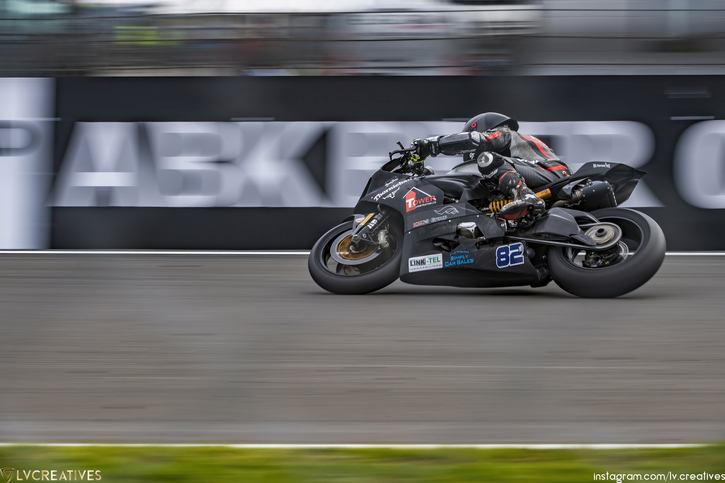 A motorcycle racer in full gear leaning into a turn on a race track, with a blurry background showing a large 'PARKER' sign.