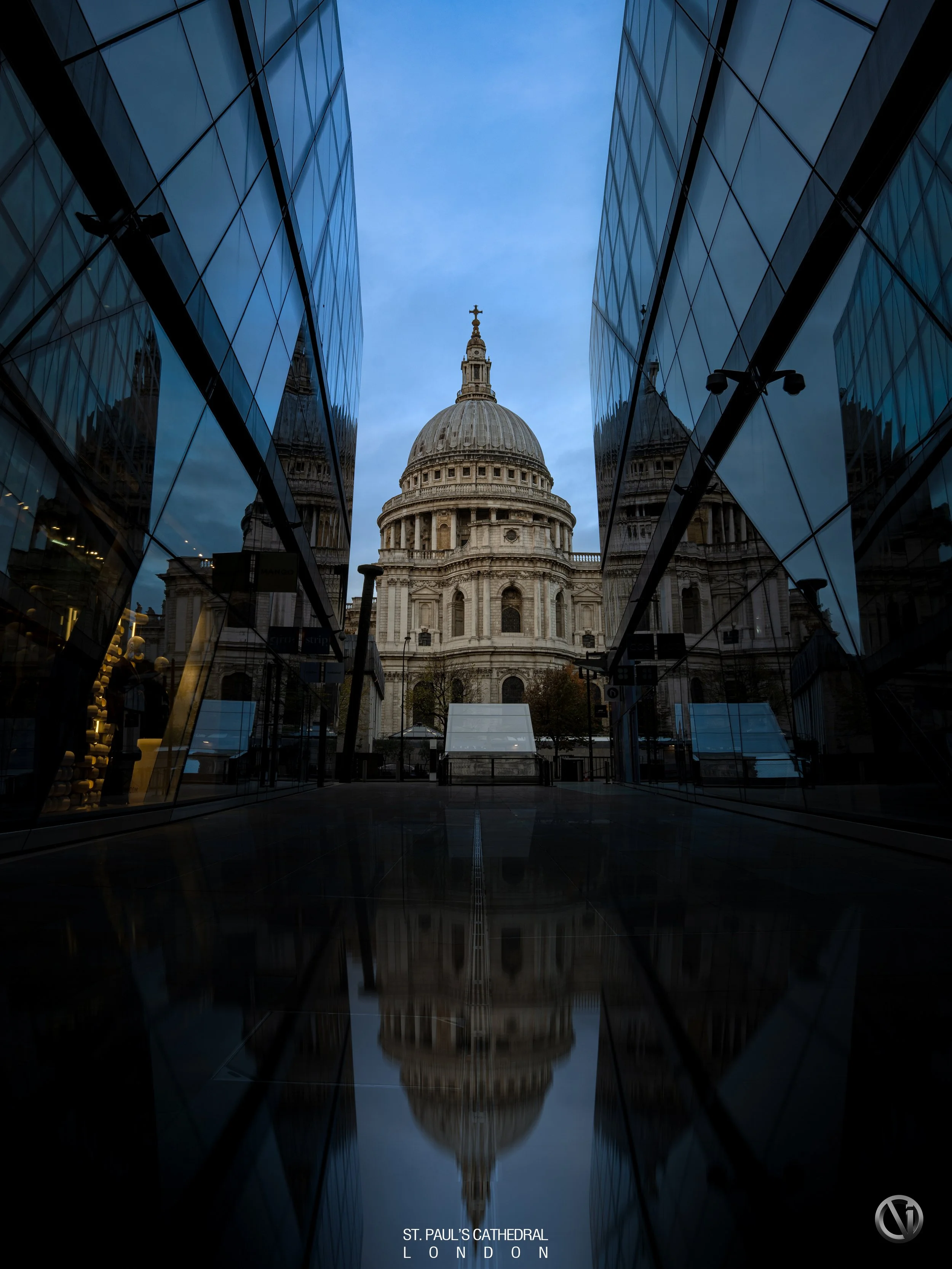 St. Paul's Cathedral in London viewed through modern glass buildings, with its reflection visible in a water feature on the ground.