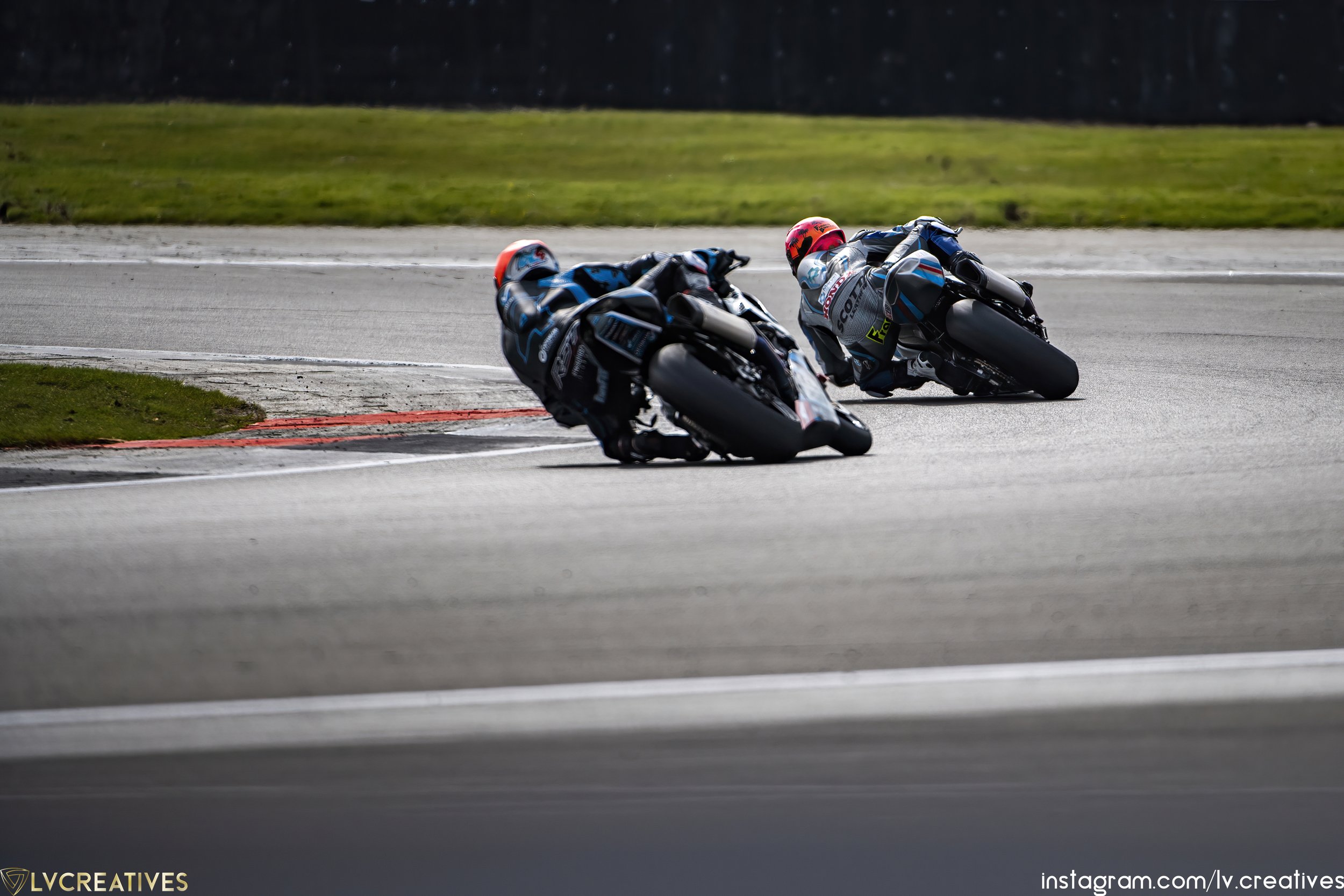 Two motorcycle racers leaning into a curve on a race track, wearing full racing gear and helmets.
