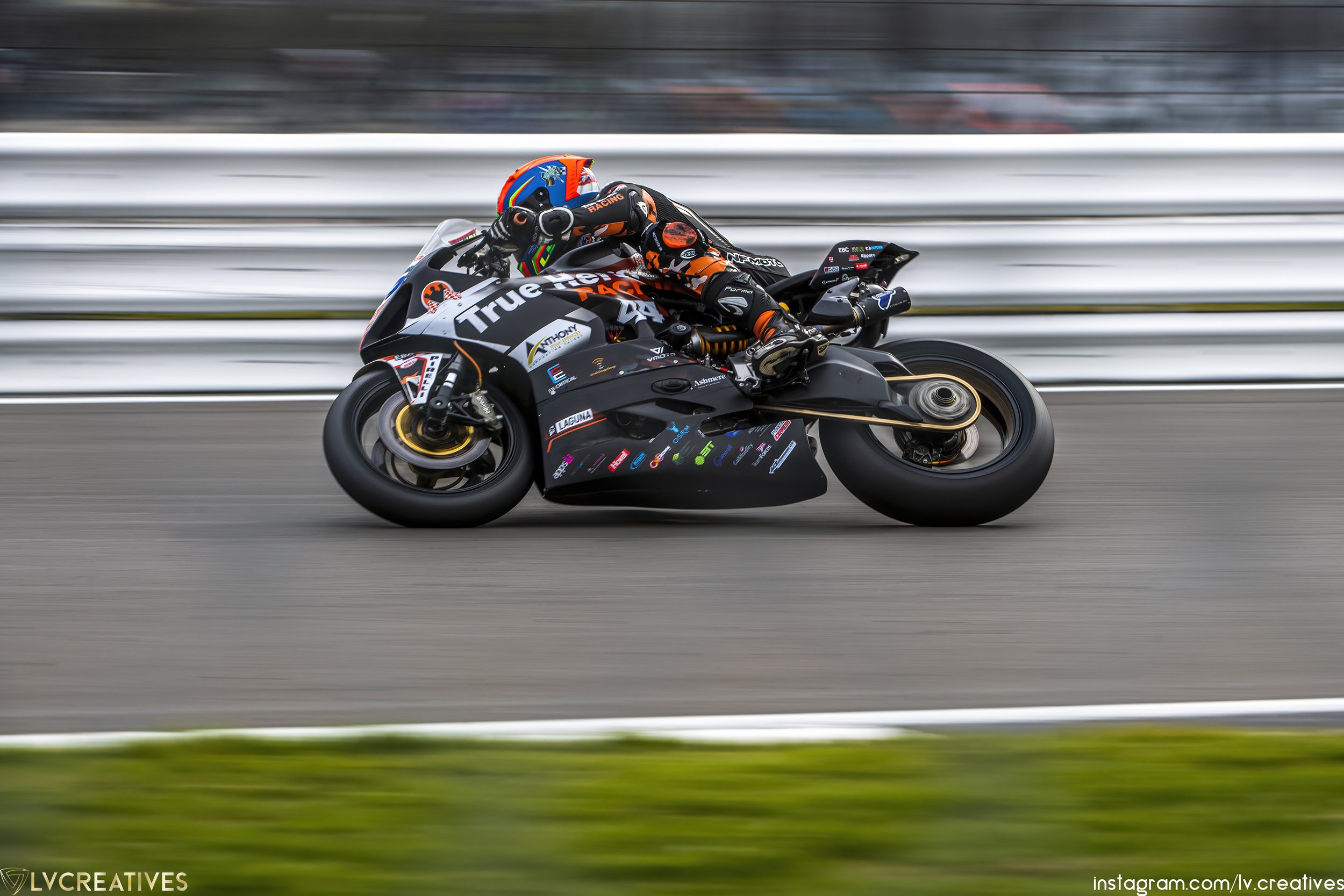 Motorcycle racer in orange and black gear leaning into a turn on a black racing motorcycle on a racetrack