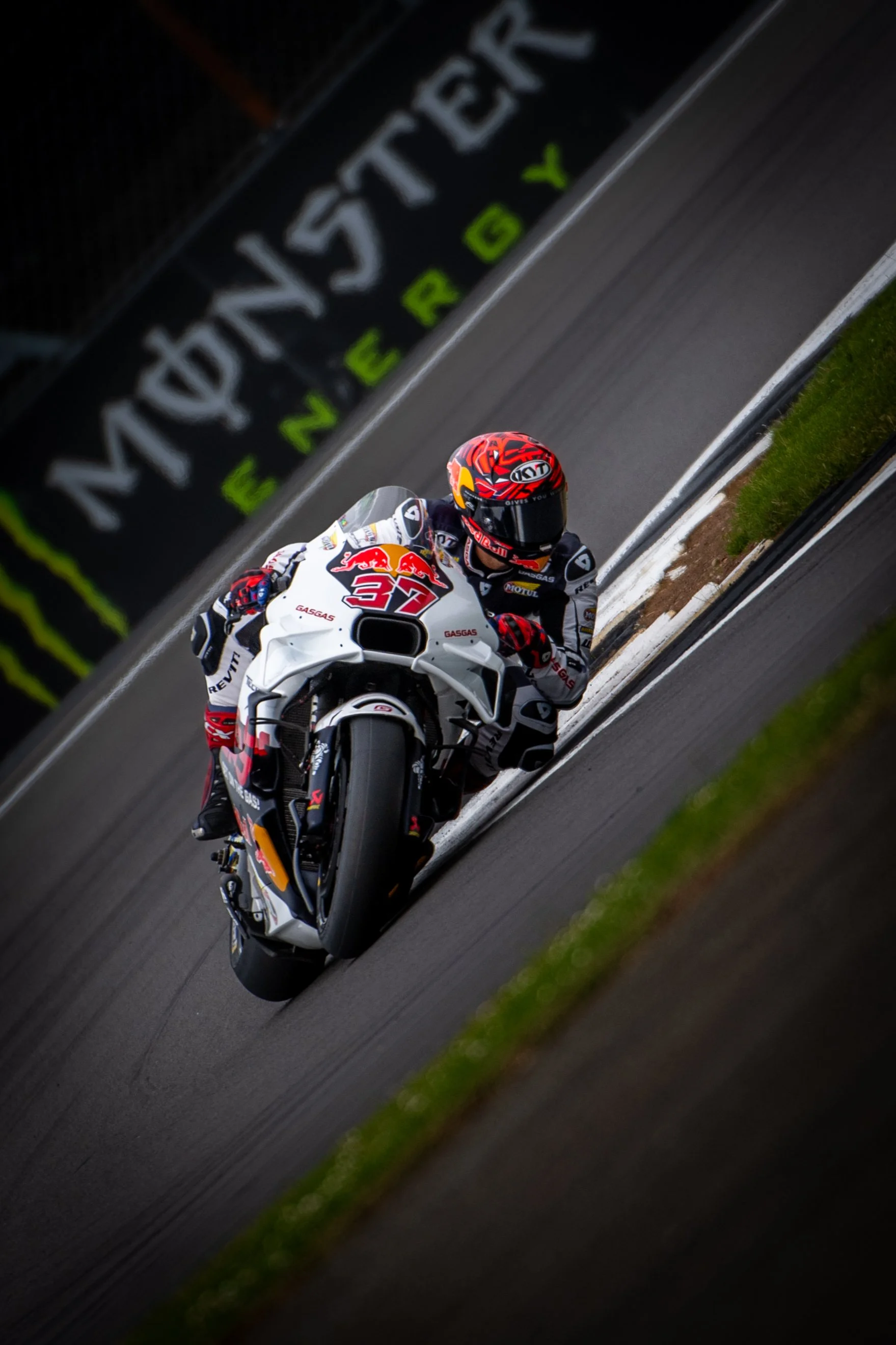 A motorcycle racer in racing gear riding a white motorcycle with Red Bull logo on a race track.