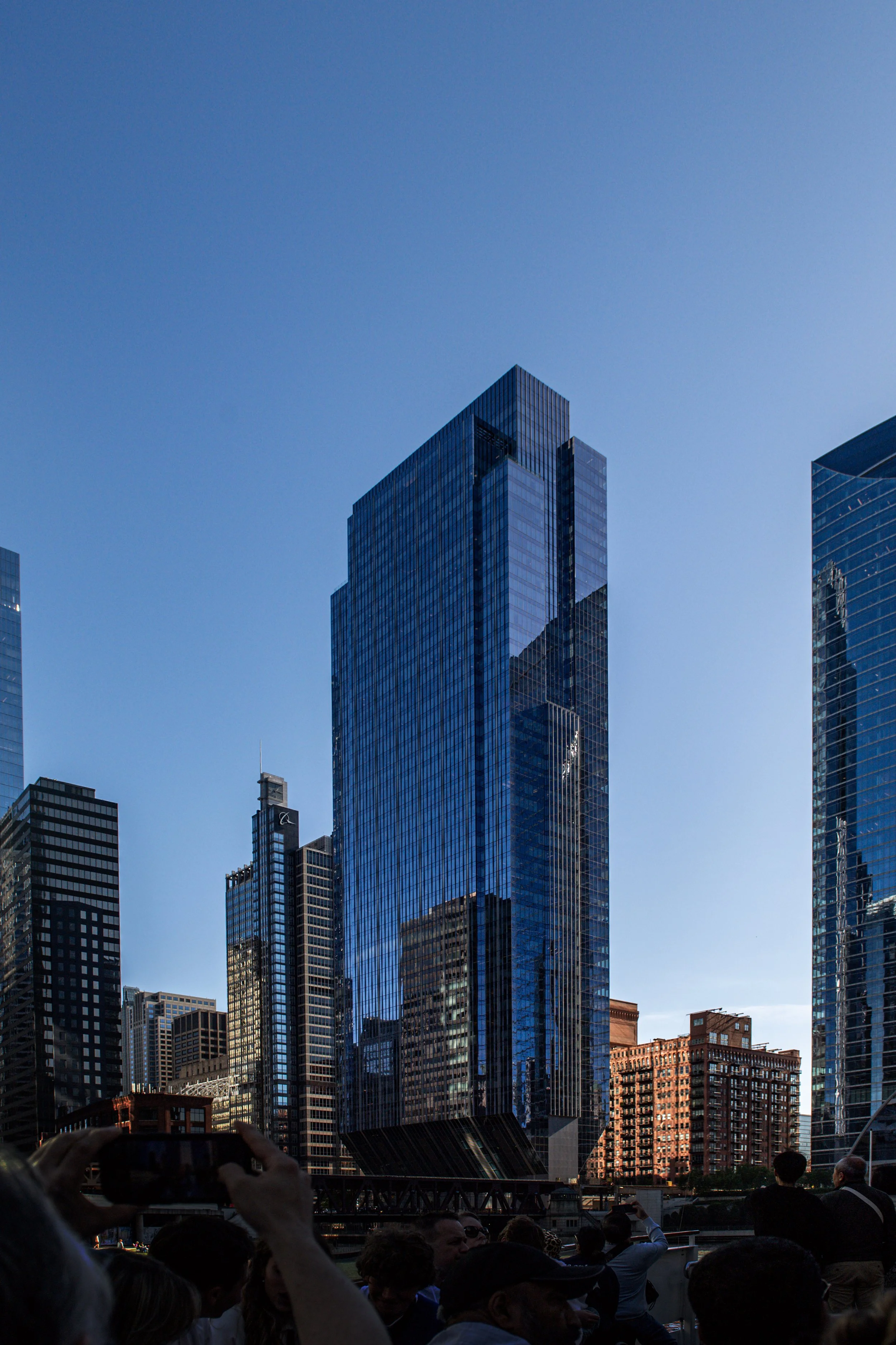 Tall, modern blue glass skyscraper in a city with a crowd of people in the foreground.