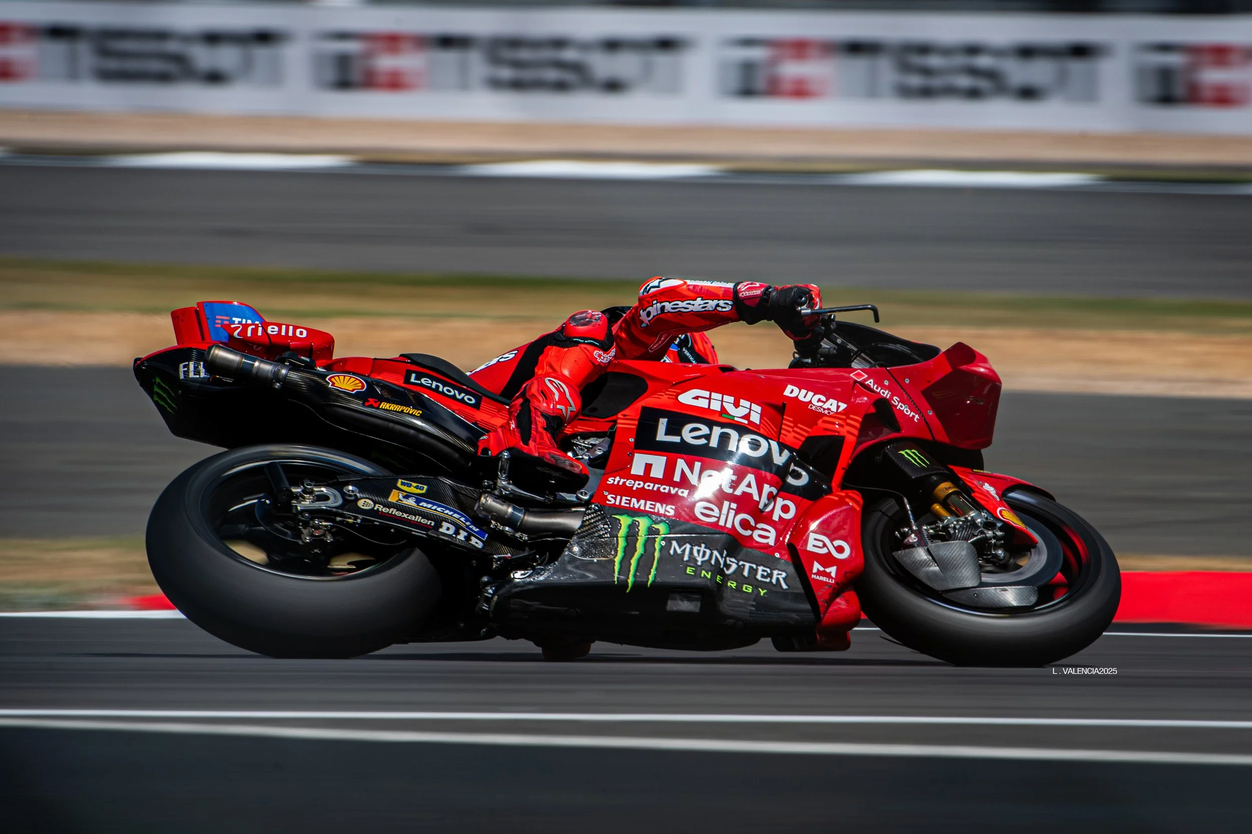 A professional motorcycle racer in red gear leaning into a turn on a red racing motorcycle on a race track.