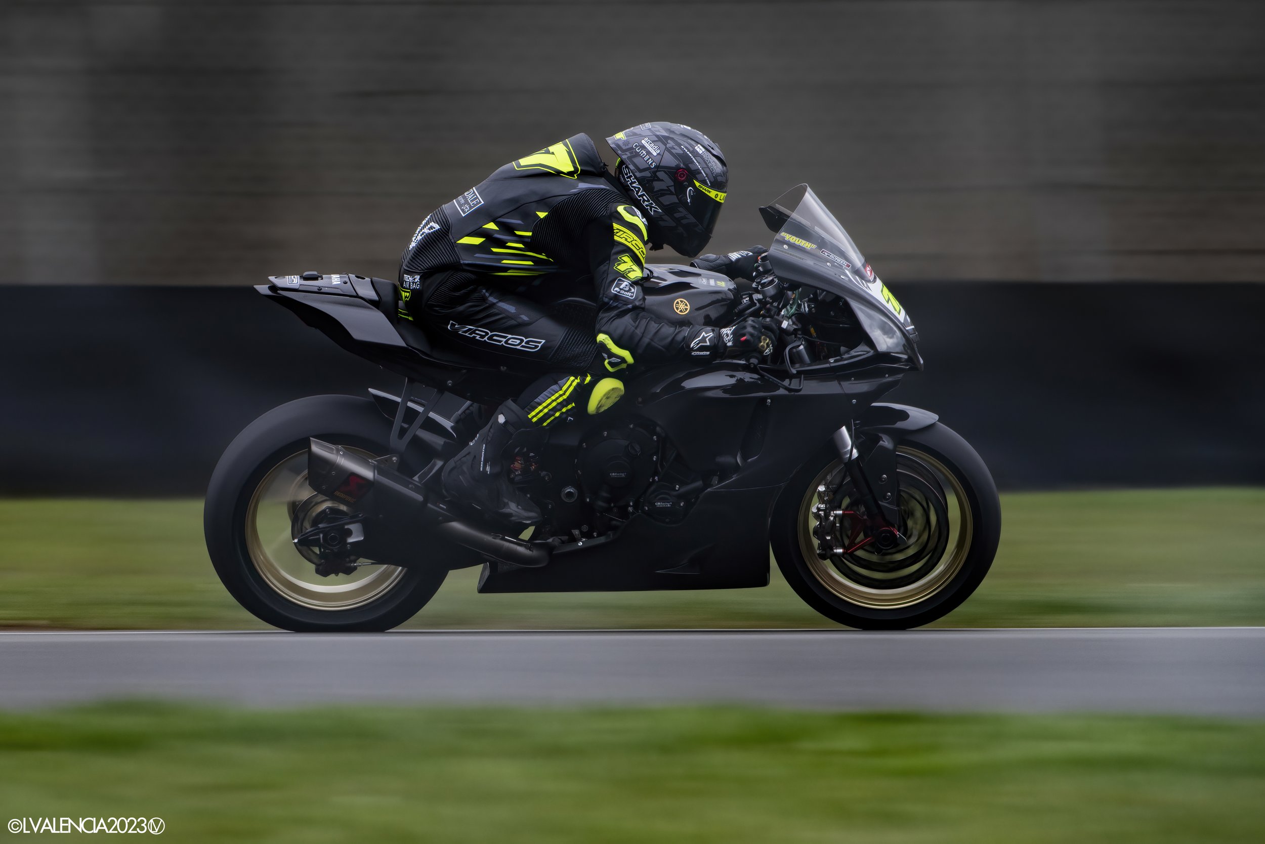 Motorcyclist in racing gear riding a black sportbike on a track, with a blurred background indicating high speed.