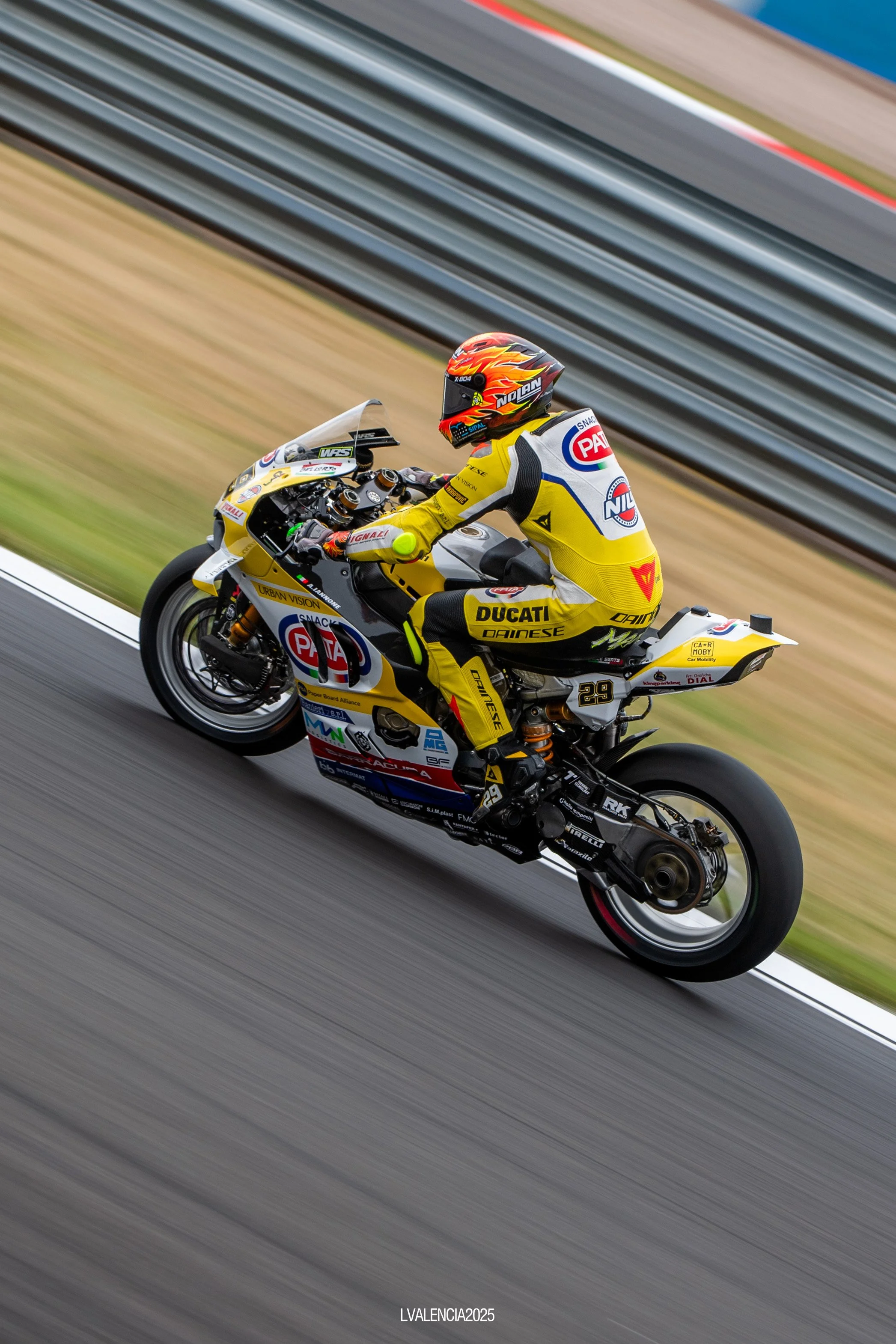 Motorcycle racer in yellow racing suit riding on a race track with colorful sponsor logos and the number 29