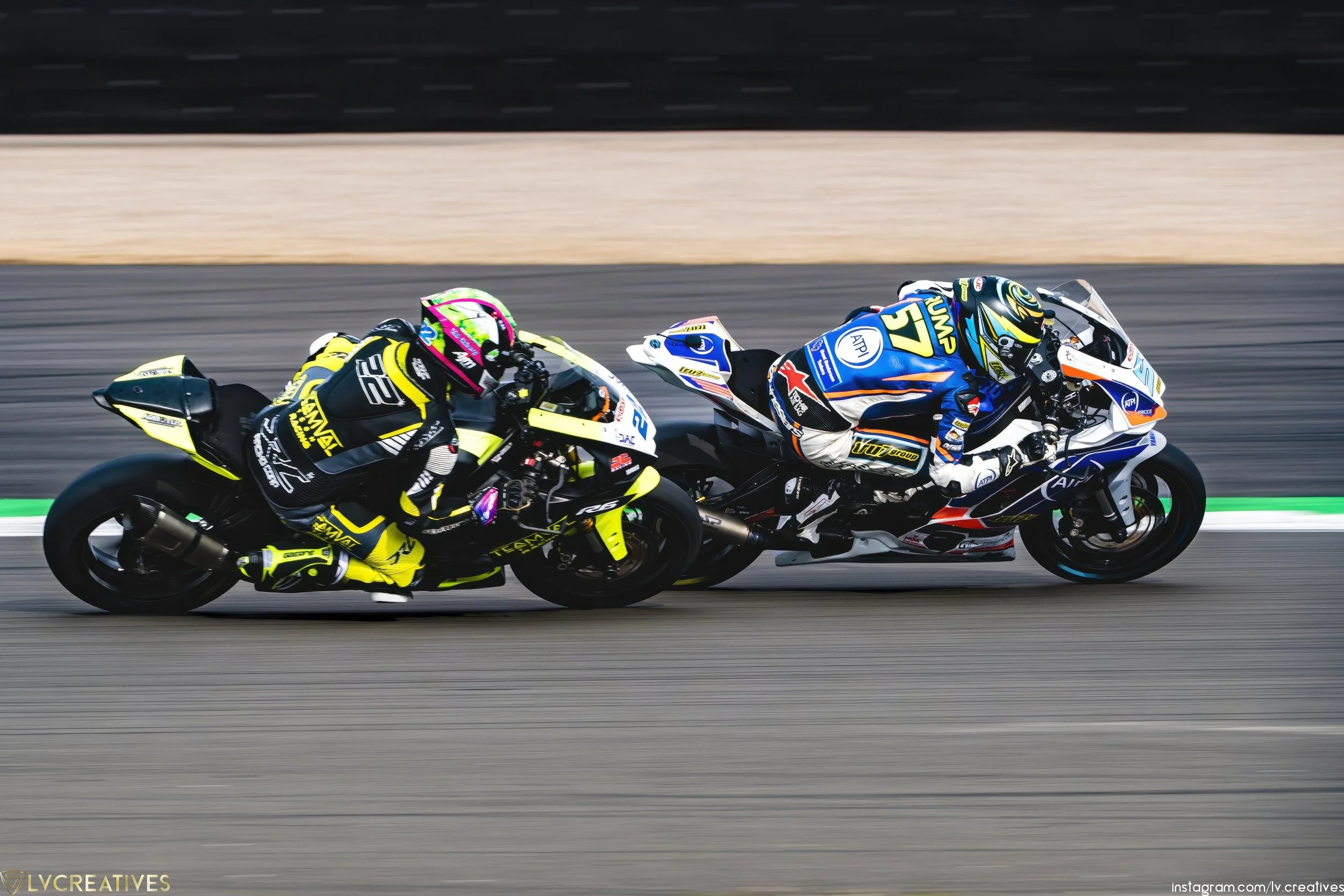 Two motorcycle racers leaned into a turn on a race track, with the rider on the left wearing a black and yellow suit and helmet, and the rider on the right wearing a blue and white suit with a yellow helmet.