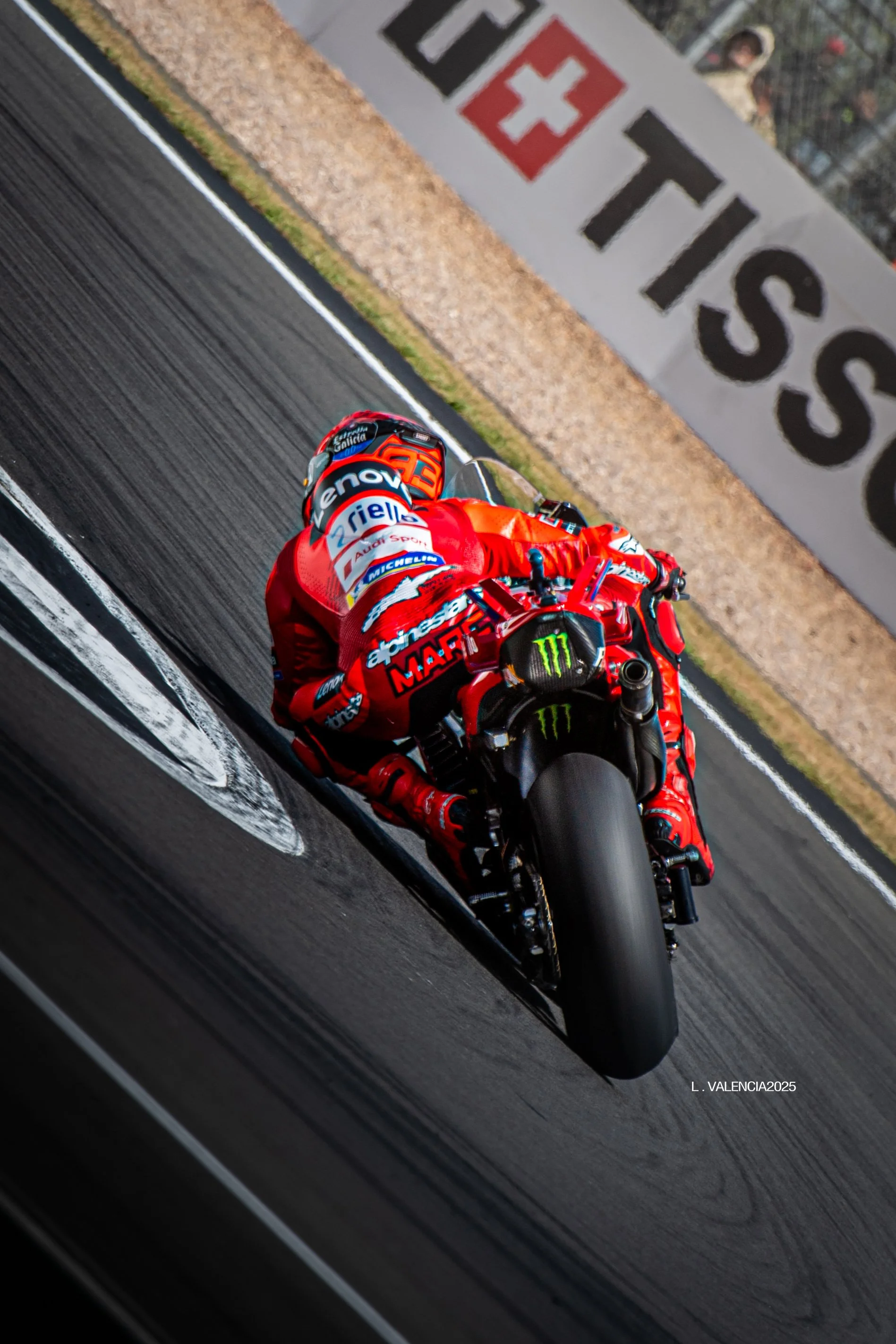 A professional motorcycle racer in red racing suit and helmet riding a red motorcycle on a race track during a competition.