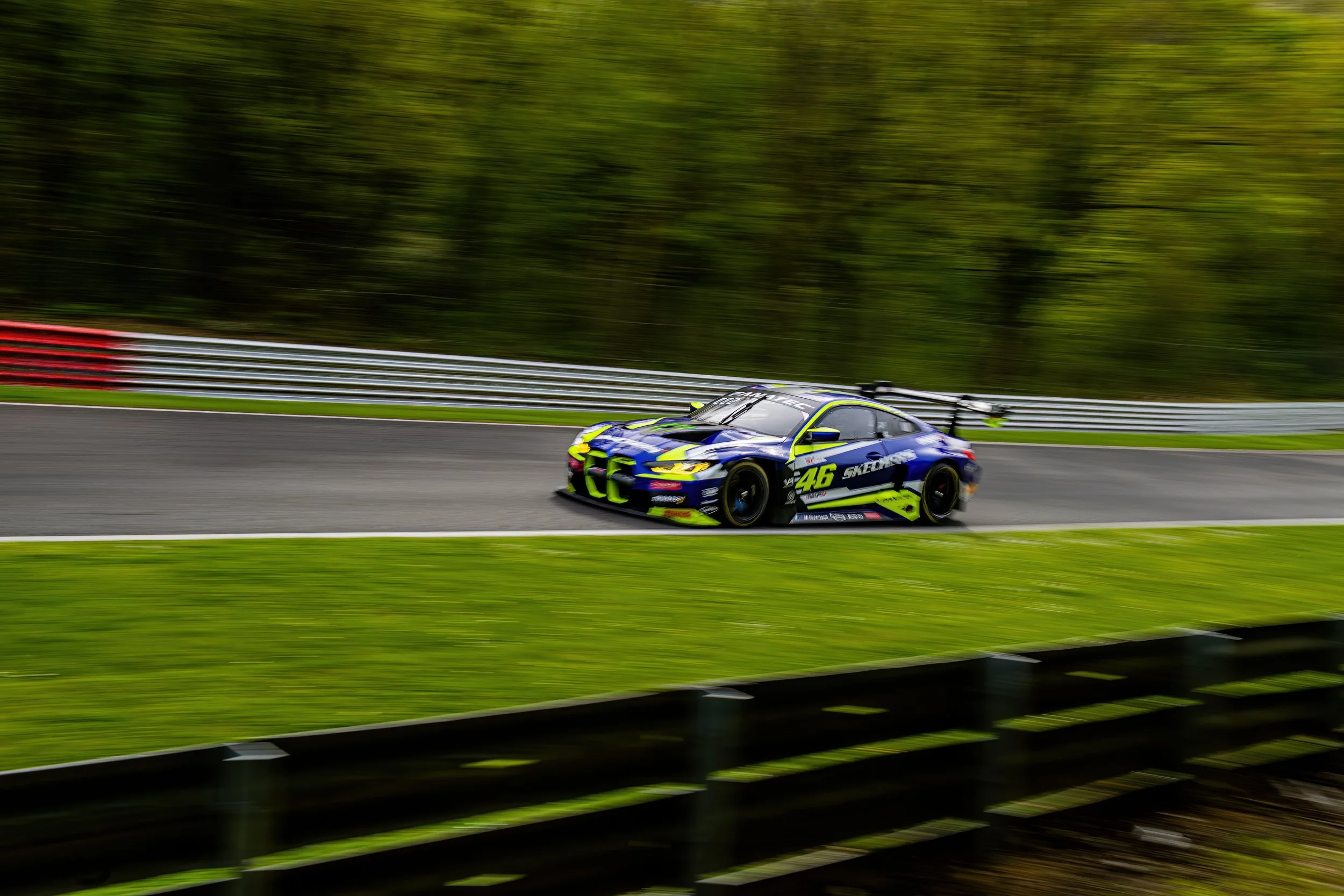 A blue and yellow race car speeding on a racetrack with a blurred background and greenery around.