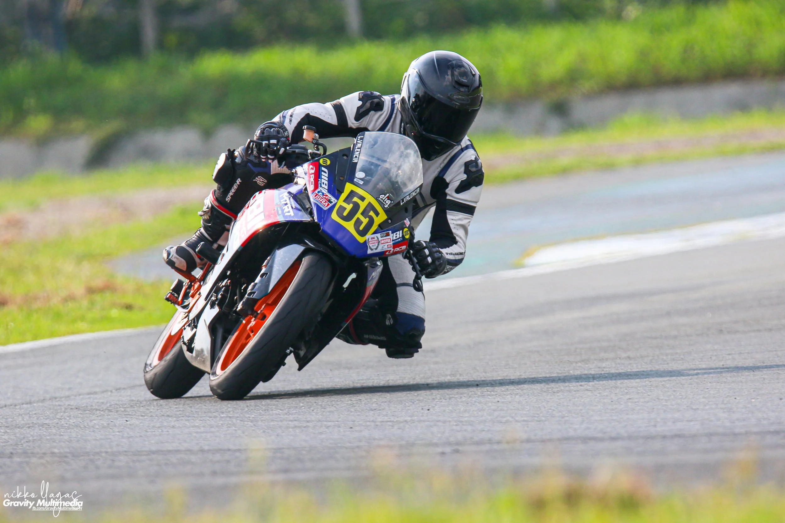 Motorcycle racer wearing black helmet and racing suit leaning into a turn on a racetrack, number 55 on the bike.  rider name Lawrence Valencia
