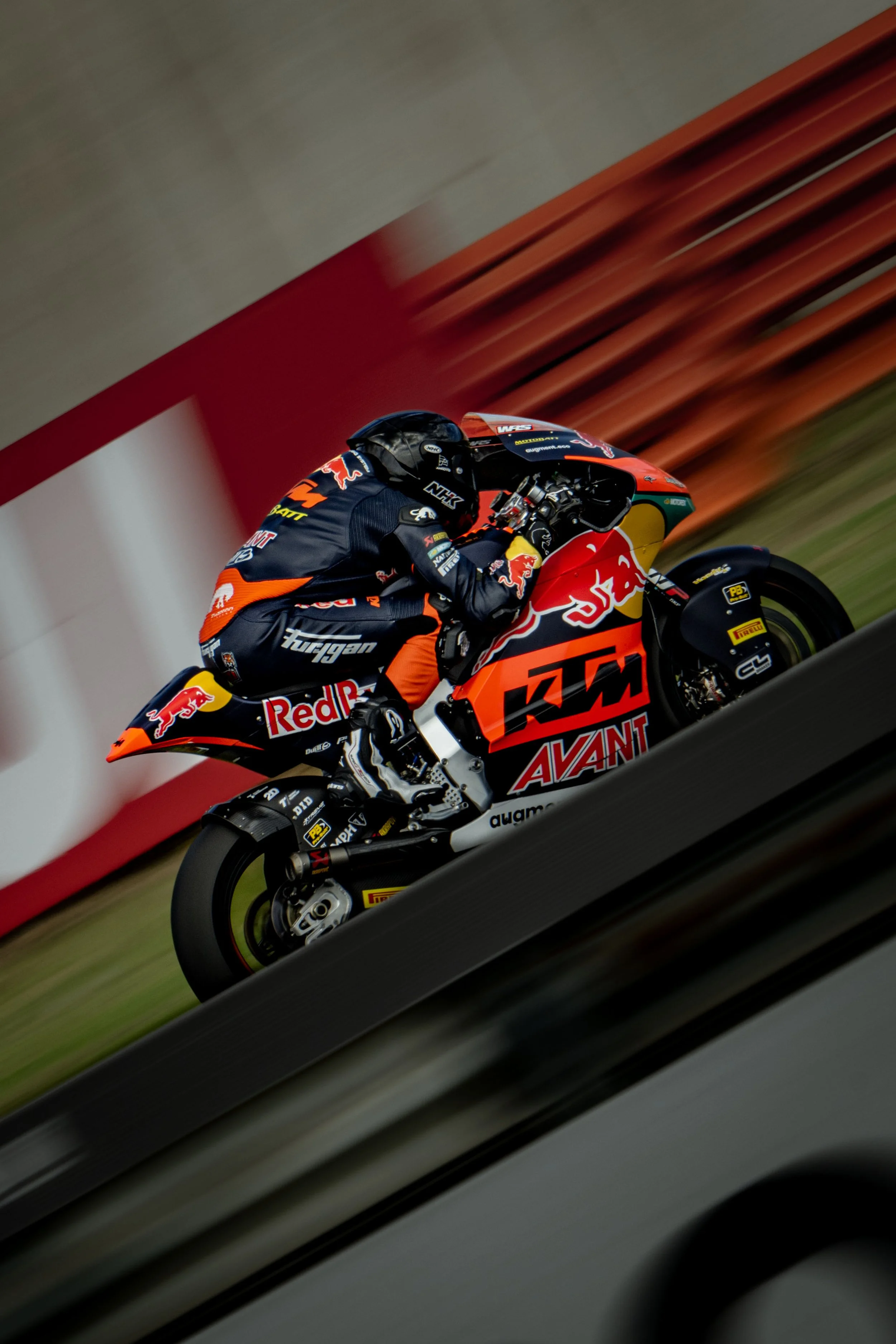 A motorcycle racer in a Red Bull KTM team suit riding a KTM race bike during a race on a race track.