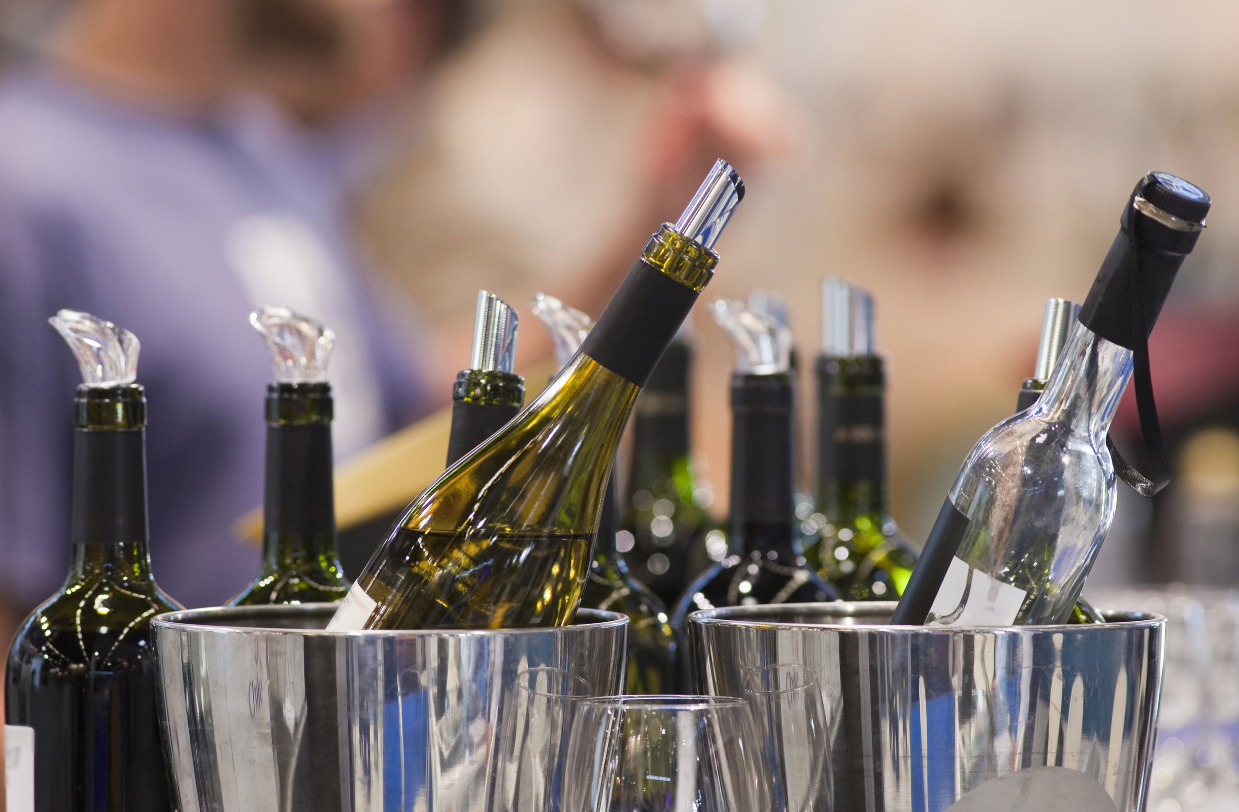 Assorted wine bottles in ice buckets, some with glass decanters, at a social event or bar.