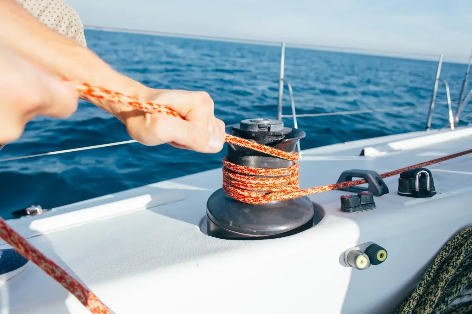 Close up detail of hands pulling tightly on a rope around a pulley on a sailing boat. Blue ocean water and sunny conditions