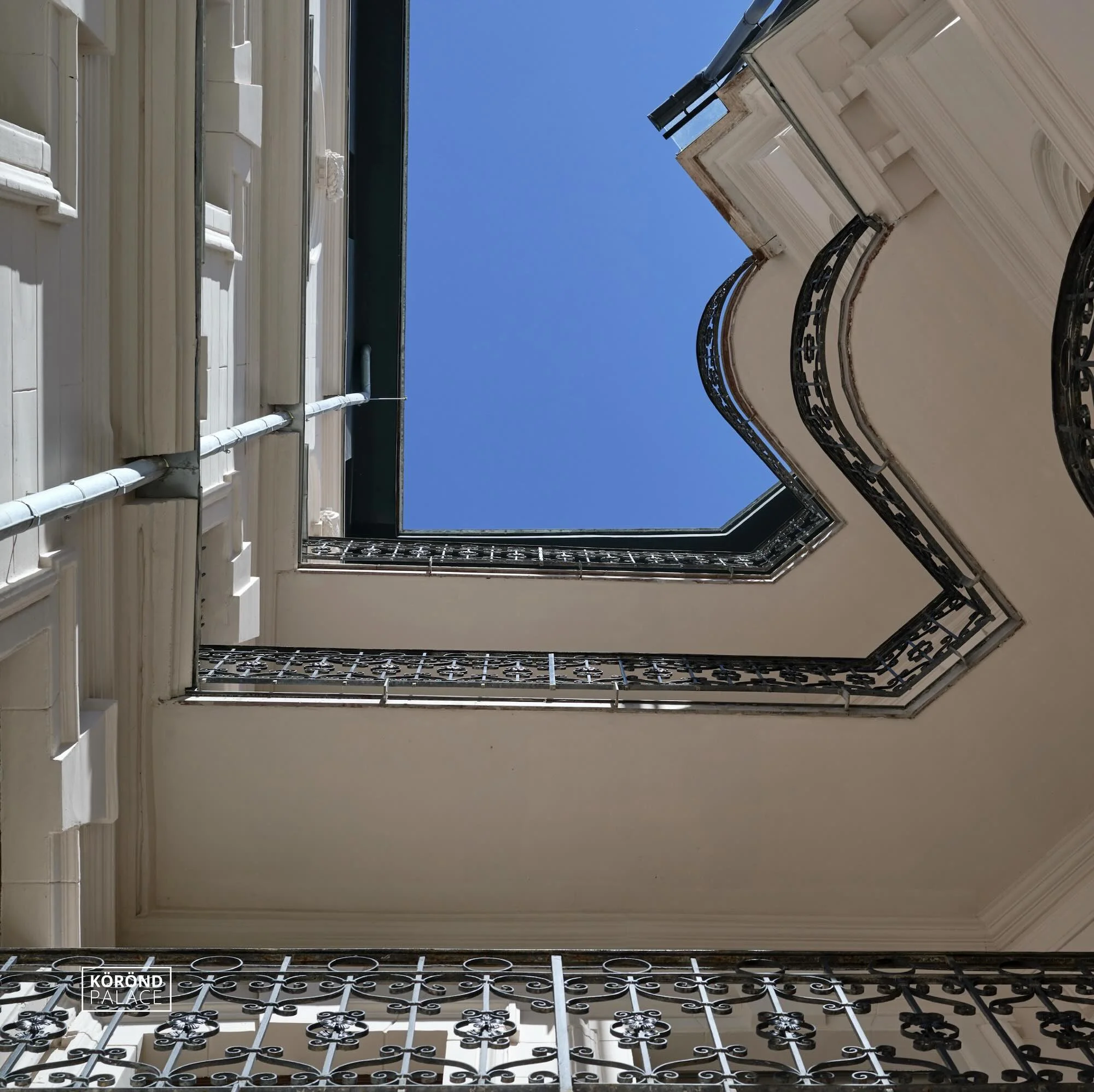Looking up at a decorative internal courtyard with wrought-iron balconies and a blue sky view.