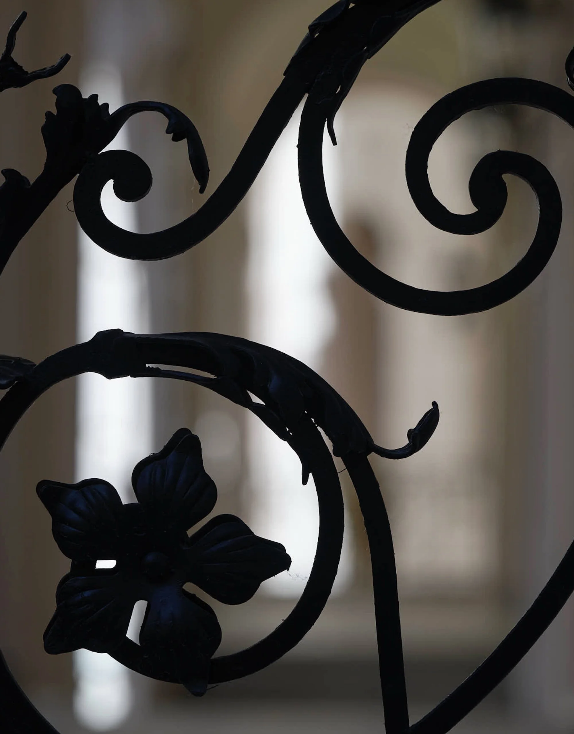 Close-up of ornate black metal scrollwork with a butterfly-shaped embellishment, against a blurred background.