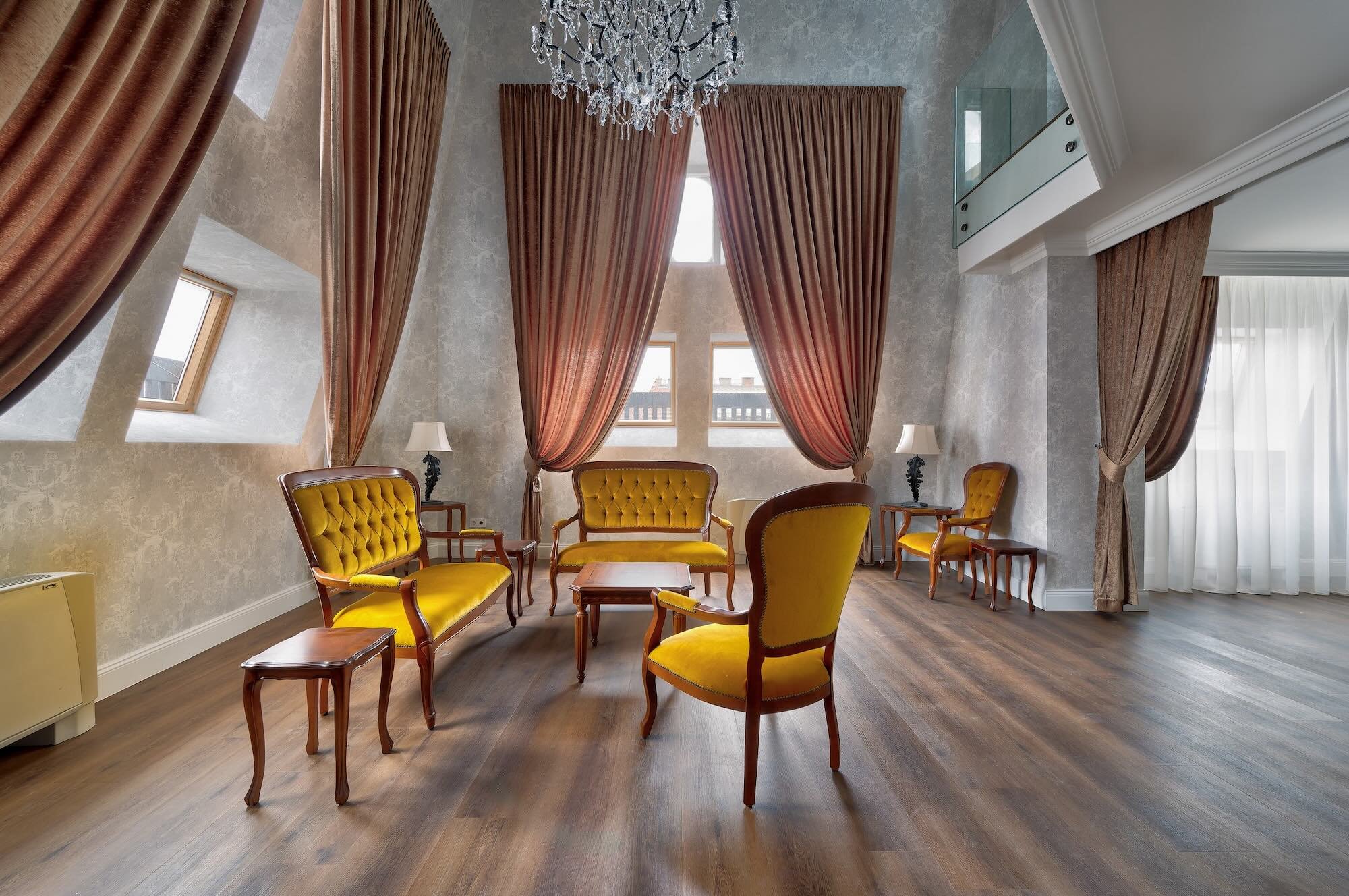 Elegant living room with vintage yellow upholstered furniture, large pink curtains, hardwood floors, chandelier, and windows with sheer white curtains
