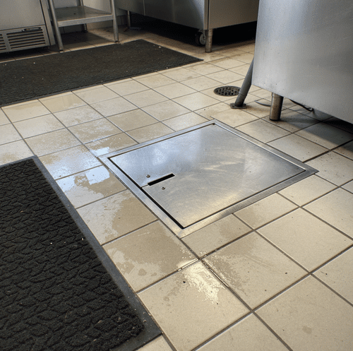 Grease trap under commercial kitchen sink being serviced