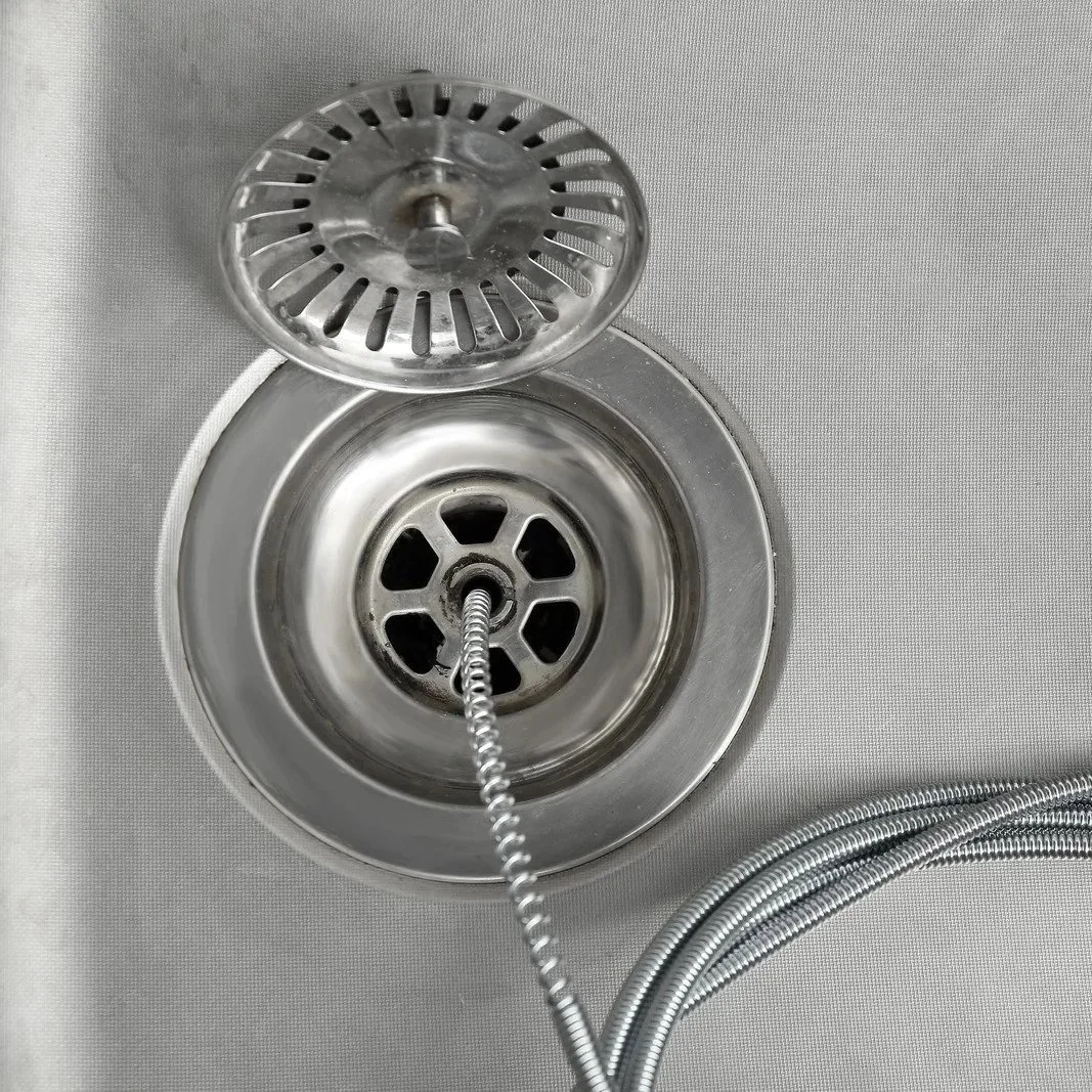 Close-up of drain snake cable inside kitchen sink drain during professional drain cleaning and hydro jetting clog removal service.