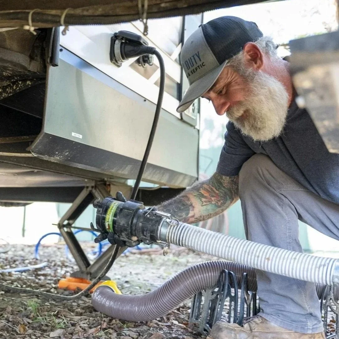 Septic technician connecting wastewater transfer hose beneath recreational vehicle during mobile septic pumping and holding tank maintenance service.