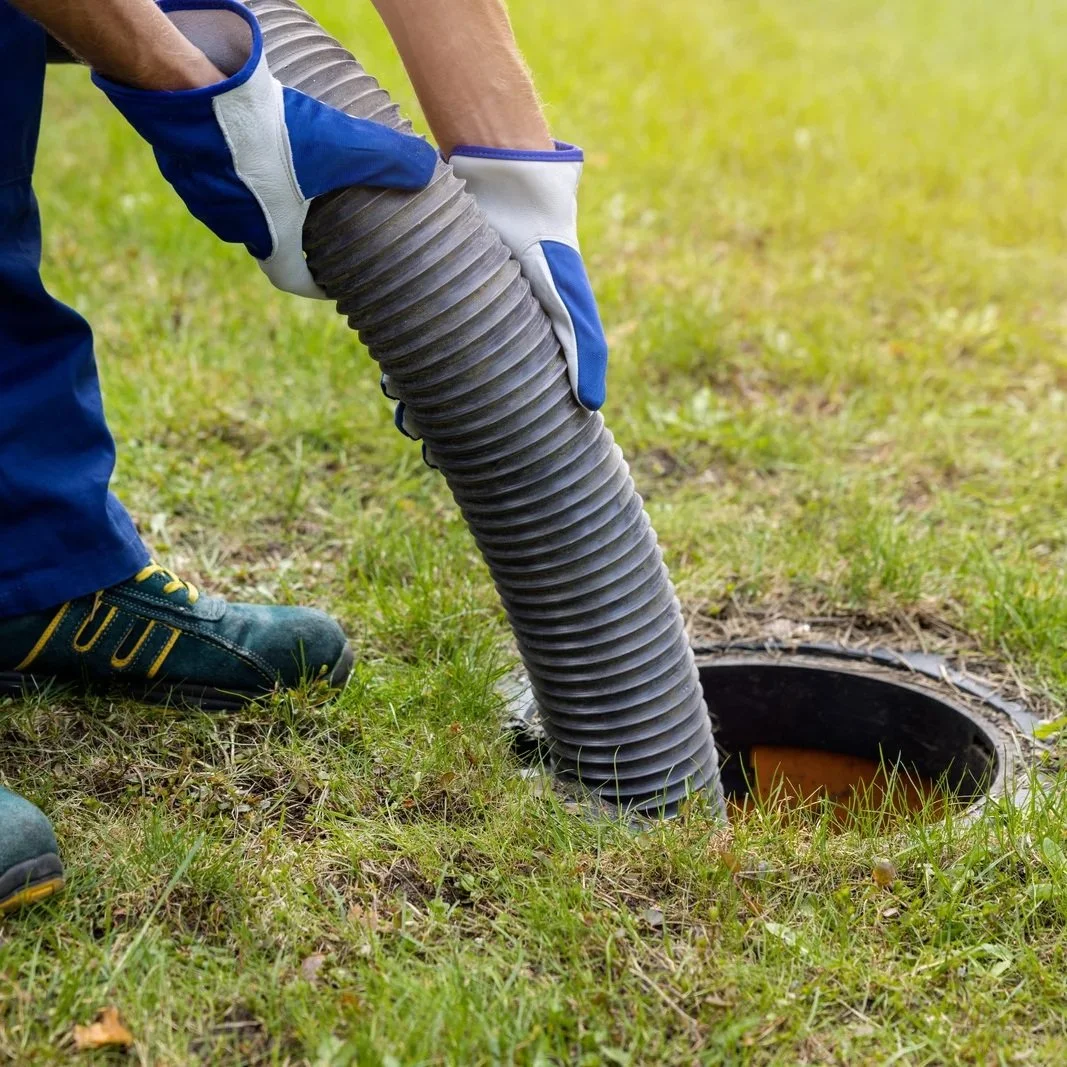 Septic pumping technician using a vacuum hose to clean a residential septic tank, illustrating professional drain and clog removal compared to temporary liquid drain cleaner fixes.
