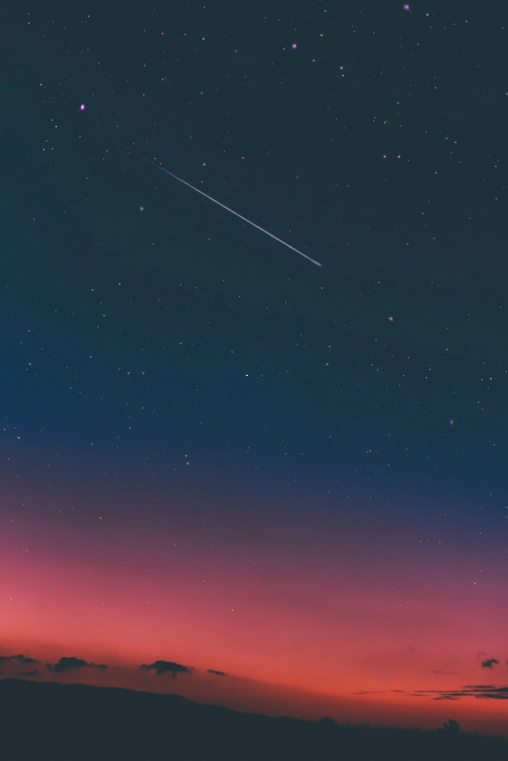A night sky with many stars, a colorful horizon with pink and purple hues, and a bright streak from a shooting star or meteor.