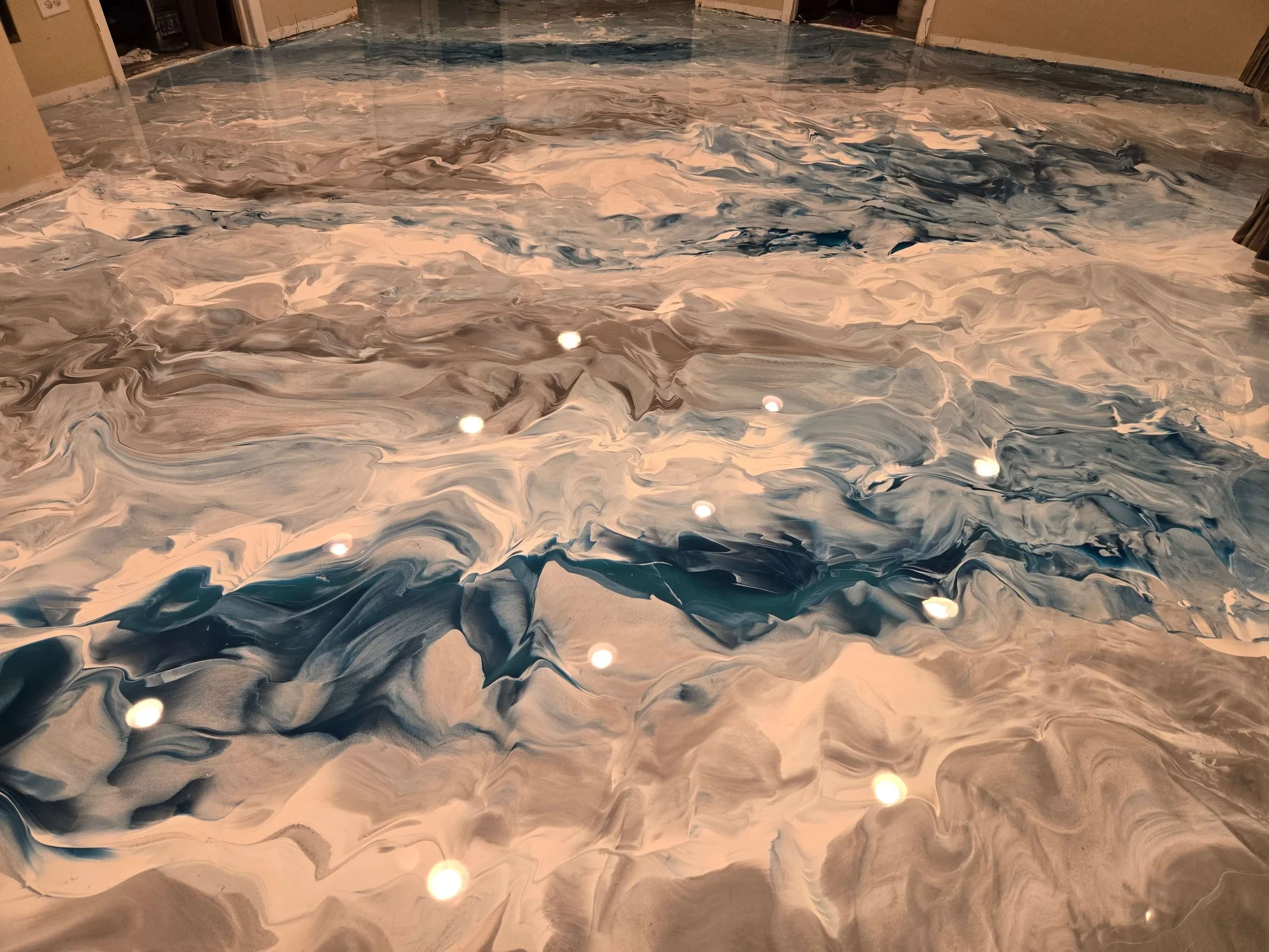 Marble-patterned resin flooring with swirling shades of white, gray, beige, and blue, reflecting overhead lights.