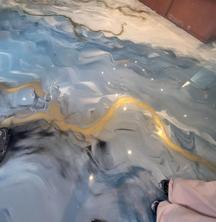Close-up view of a marble-styled resin floor with a swirling pattern in shades of black, gray, blue, white, and gold.