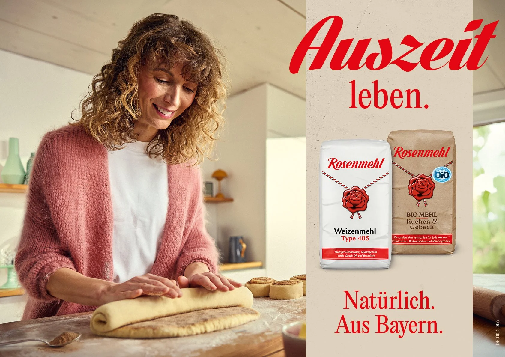 Eine Frau backt in einer Küche mit Weizenmehl und spricht fröhlich. Es stehen zwei Mehlsäcke mit der Beschriftung "Rosenmehl" auf dem Tisch, einer in weiß und einer in braun. Der Text auf der rechten Seite lautet: "Auszeit leben. Natürlich. Aus Bayern.".