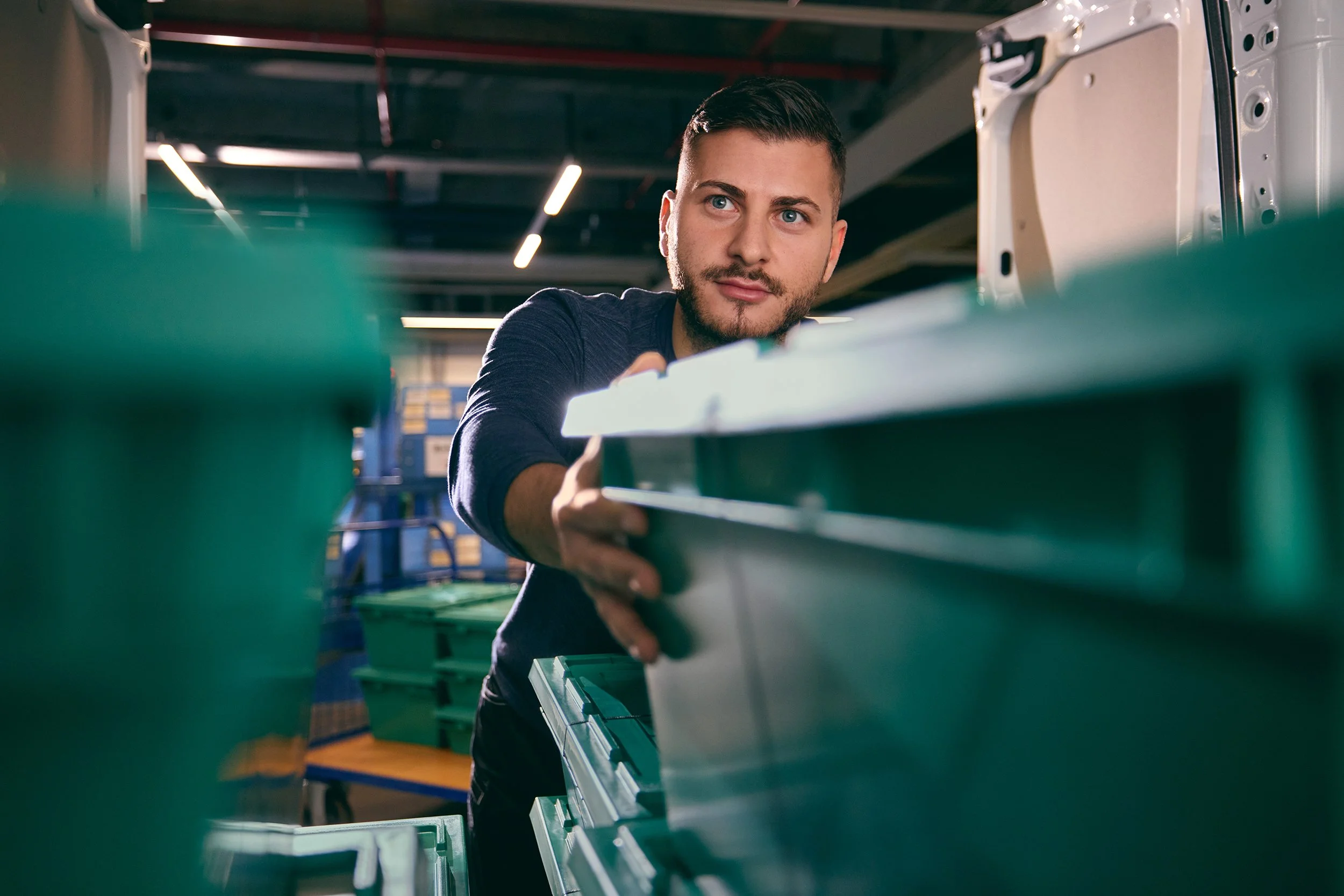 Junger Mann arbeitet in einer Werkstatt mit Grünbehältern und Werkzeugen.
