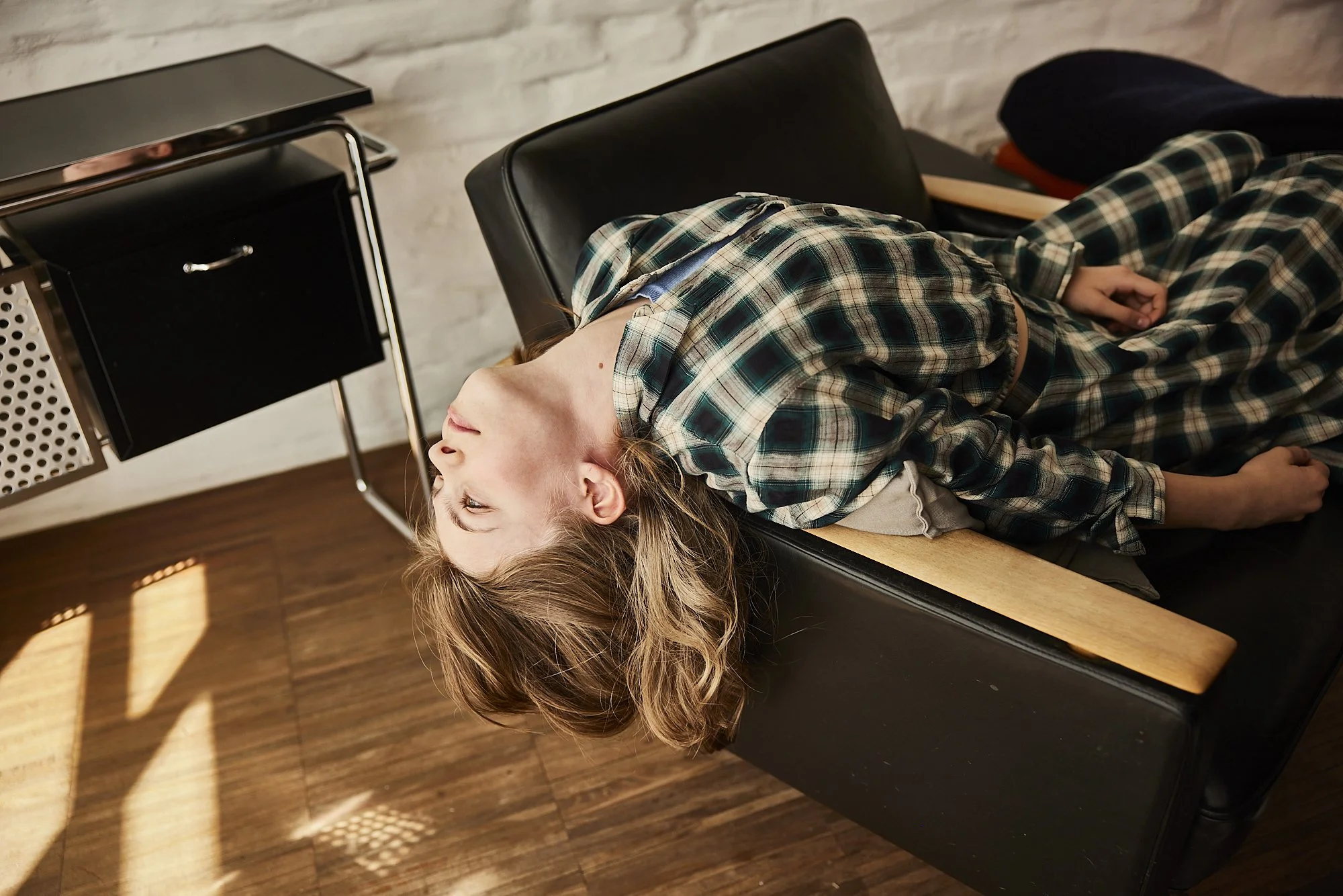 Eine junge Frau liegt regungslos auf einer schwarzen Liege in einer Arztpraxis, mit ihrem Kopf nach hinten und geöffneten Augen.