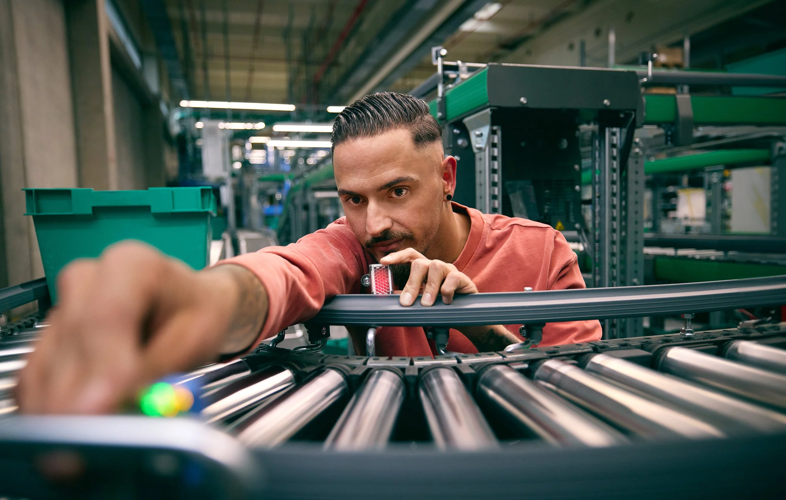 Ein Mann arbeitet in einer Industriehalle an einer Maschine mit Rollen, während er Hand anlegt.