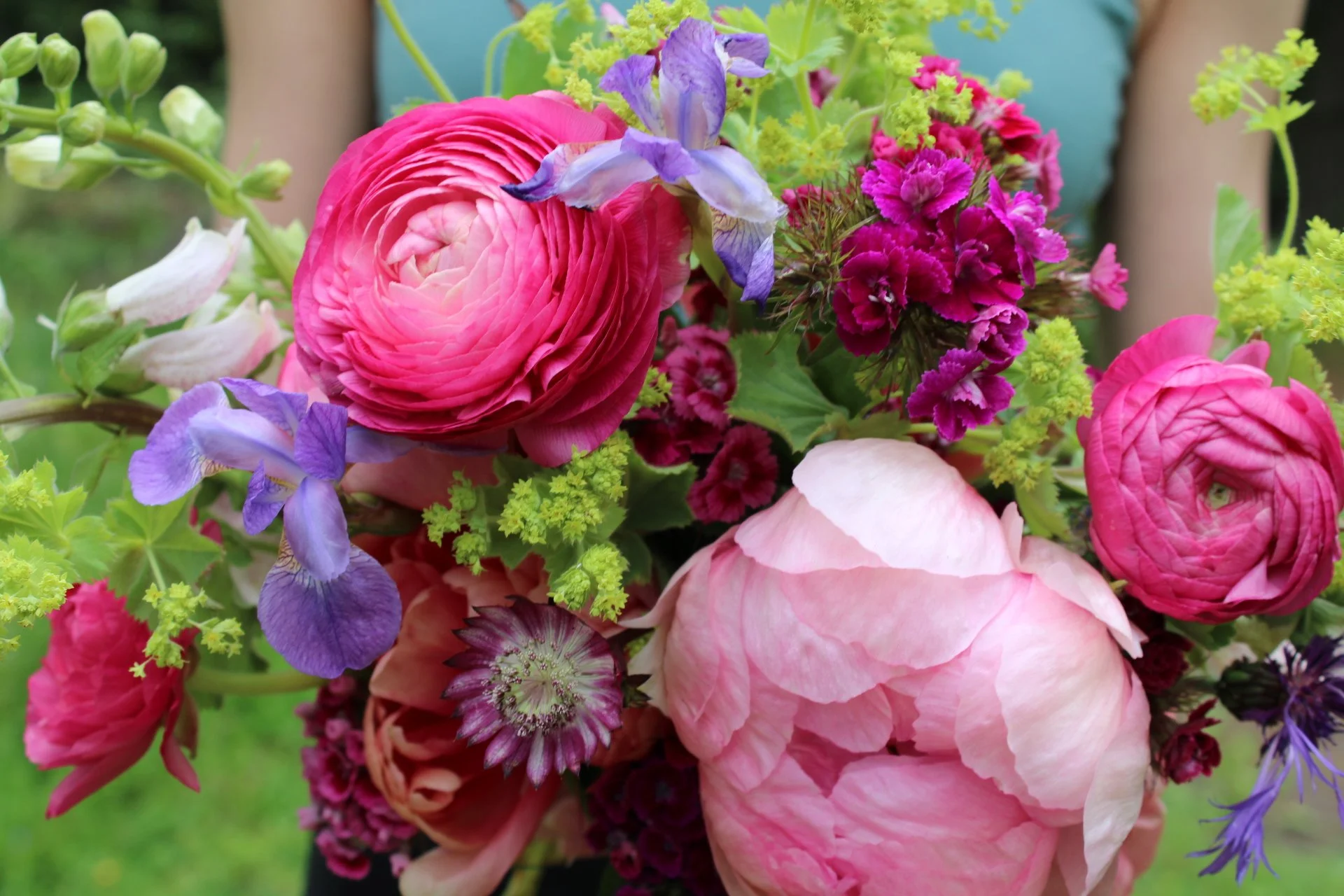 A close-up of a colorful bouquet of pink, purple, and green flowers including ranunculus and sweet peas.