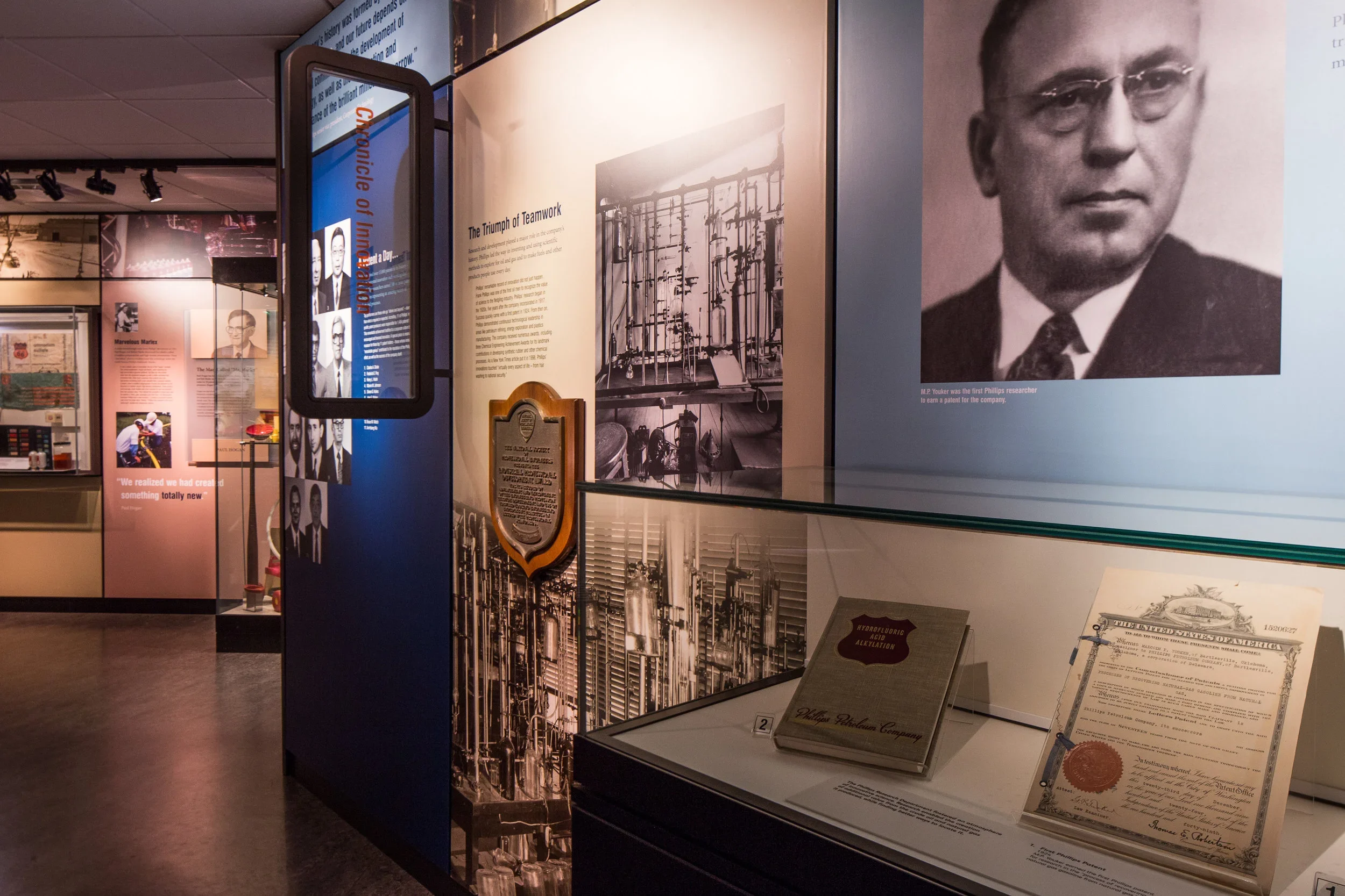 Museum exhibit with photographs, documents, and artifacts related to technological achievements and scientific figures, featuring a large portrait of a man wearing glasses and a suit.
