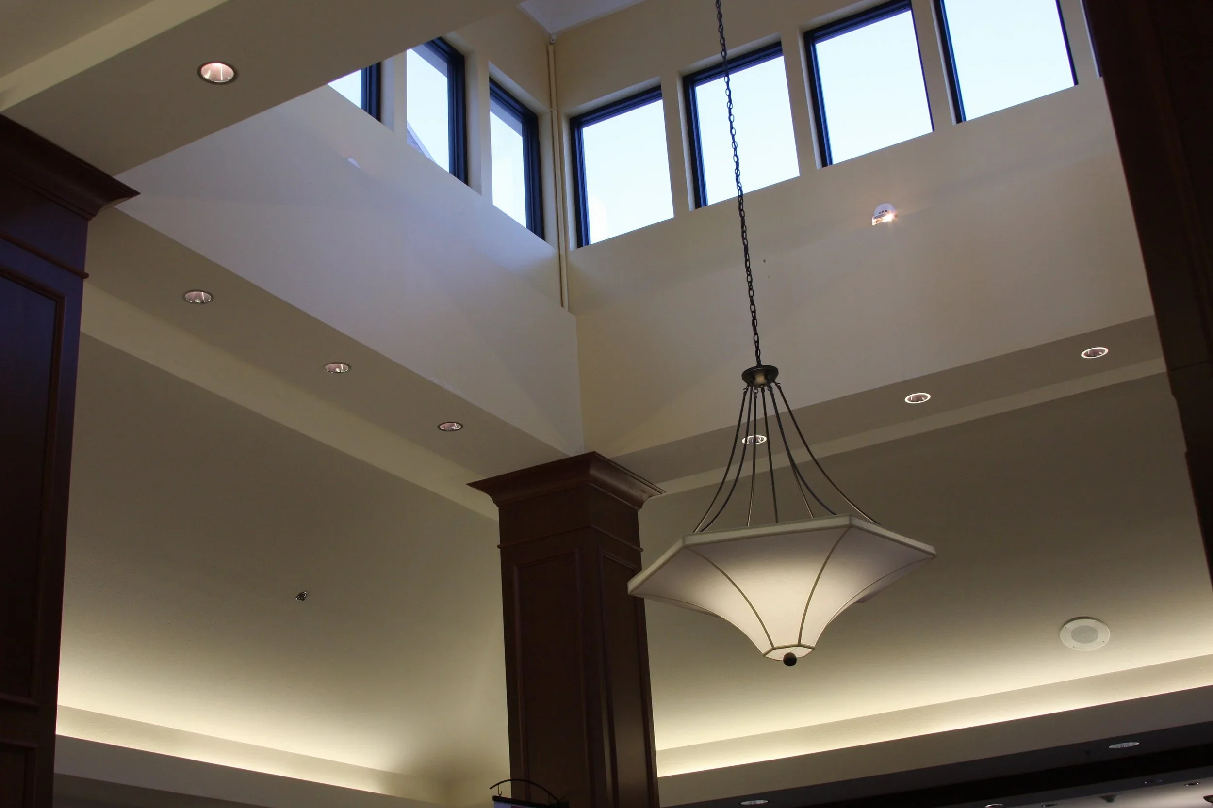 Interior ceiling view with large skylight windows, wooden columns, and a hanging chandelier light fixture.