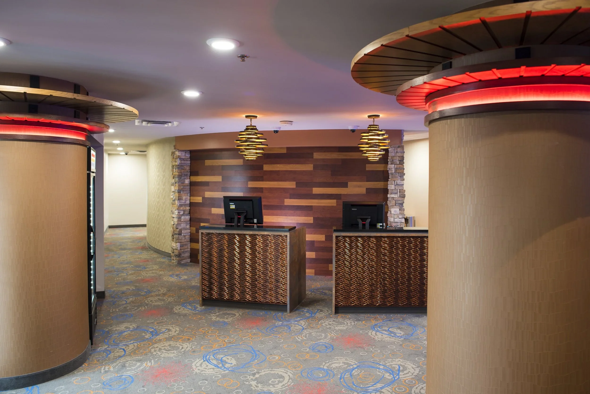 Front desk reception area in a hotel lobby with two computer monitors, decorative wall, and hanging light fixtures.