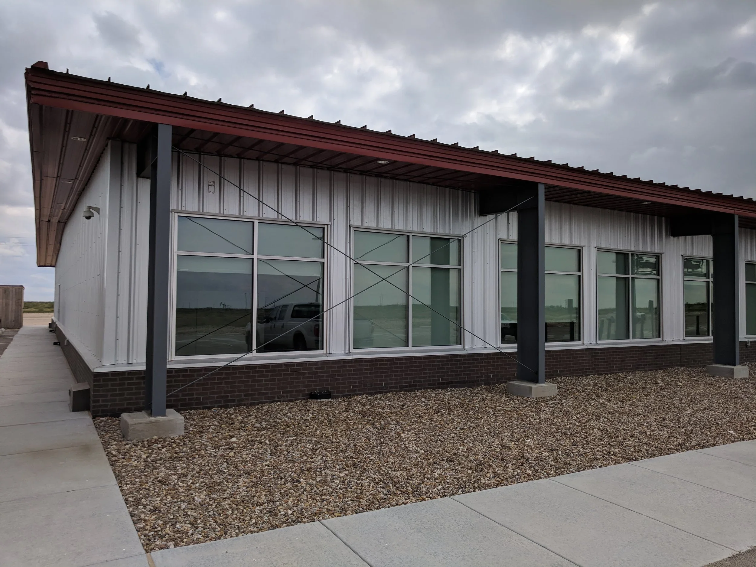 Modern single-story building with large glass windows, metal siding, and brick foundation, under a cloudy sky.