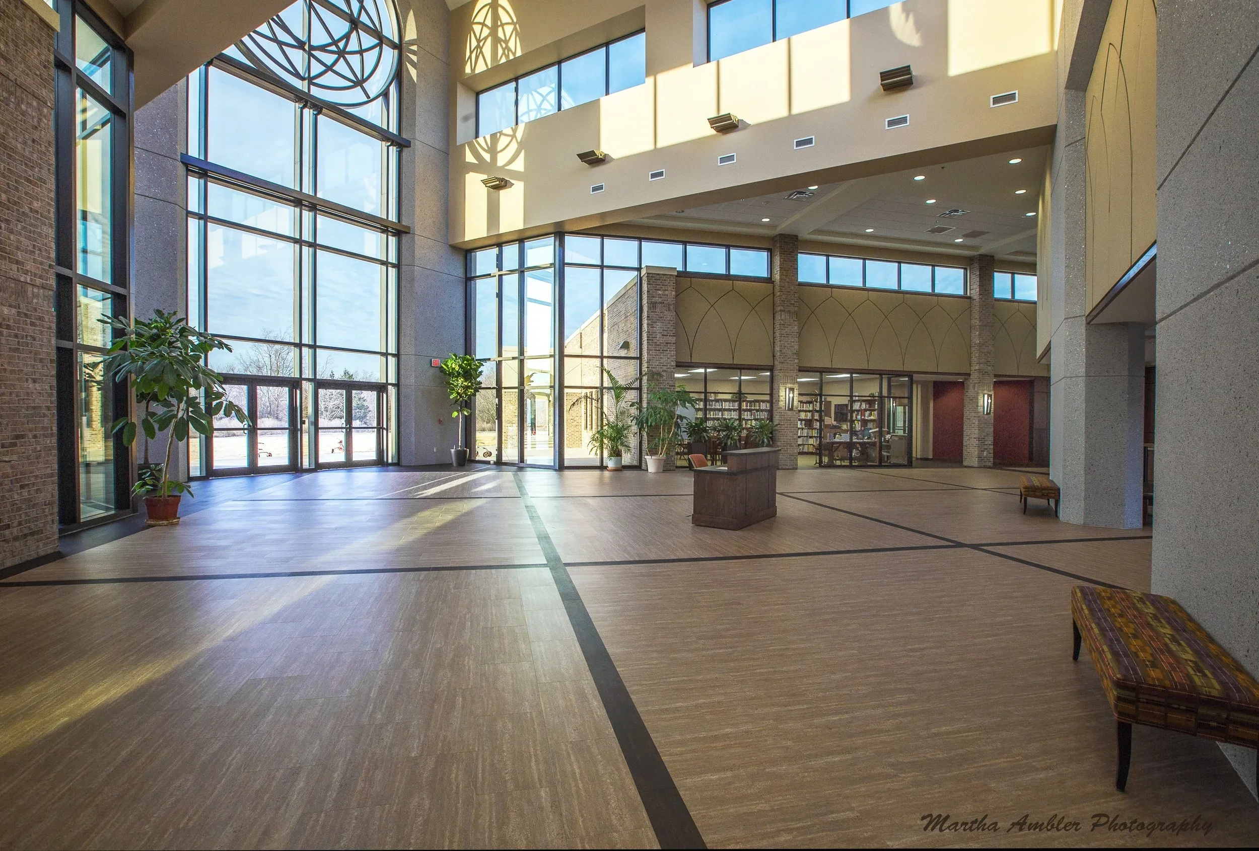 Spacious lobby with large glass windows, potted plants, wooden floors, and seating area.