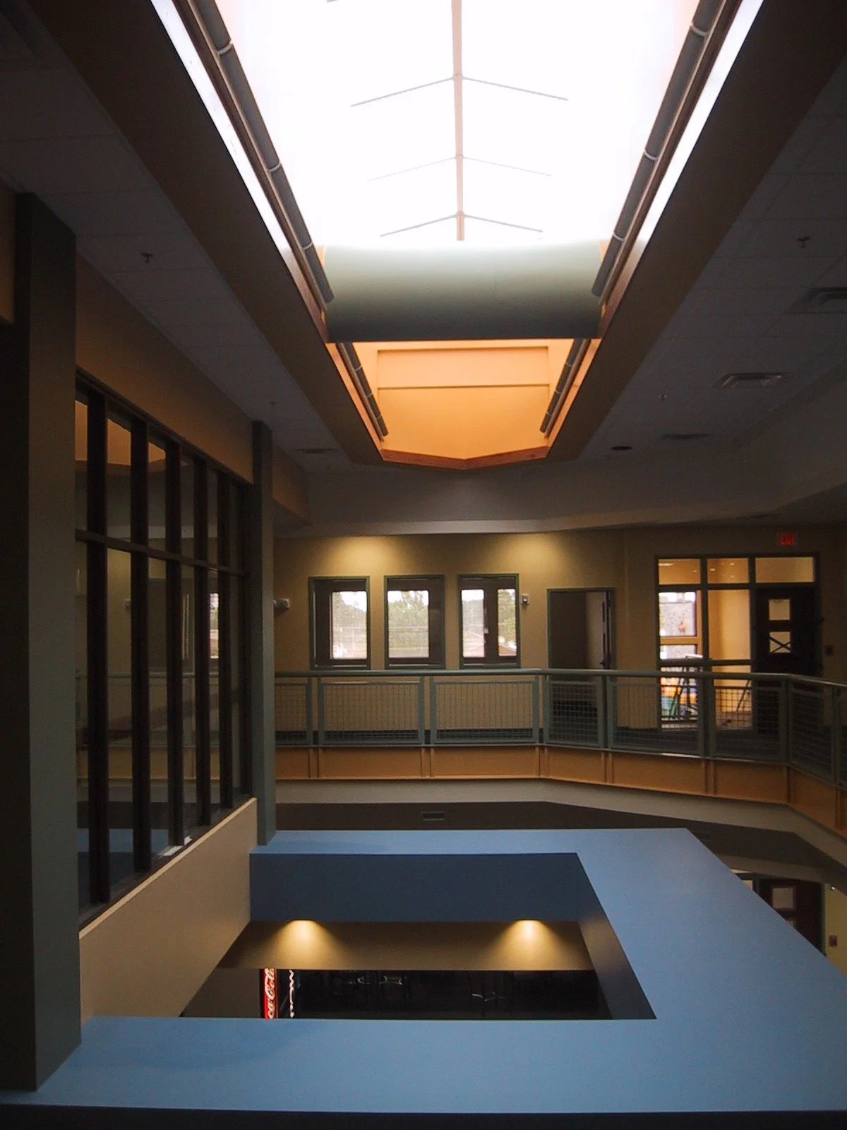 Interior of a multi-story building with an open central area, featuring a large skylight on the ceiling and windows on the walls, with a railing around the upper level.