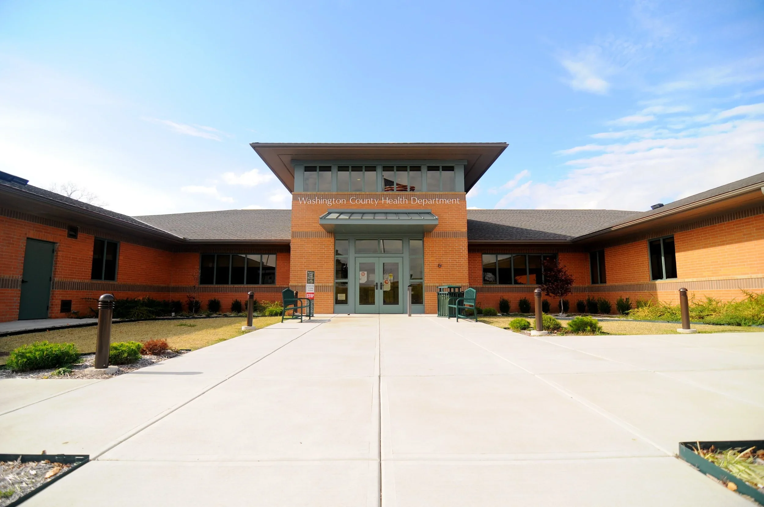 Exterior of Washington County Health Department building with brick walls, glass doors, and a small landscaped front yard on a sunny day.