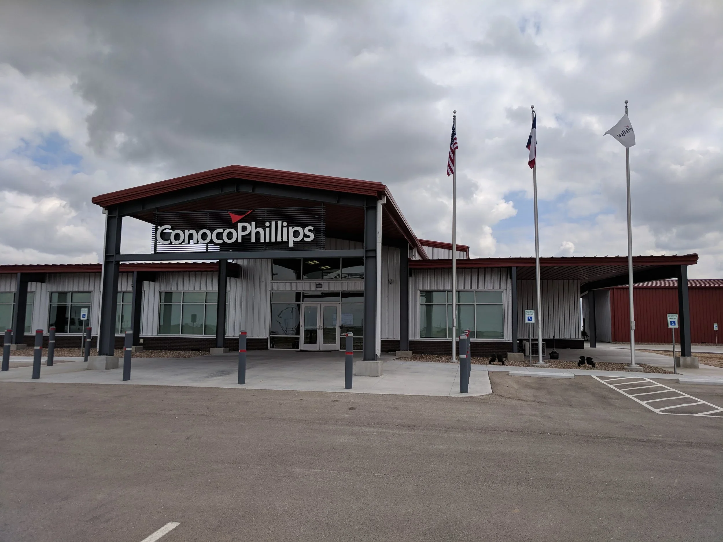ConocoPhillips office building with flags, parking lot, and cloudy sky.