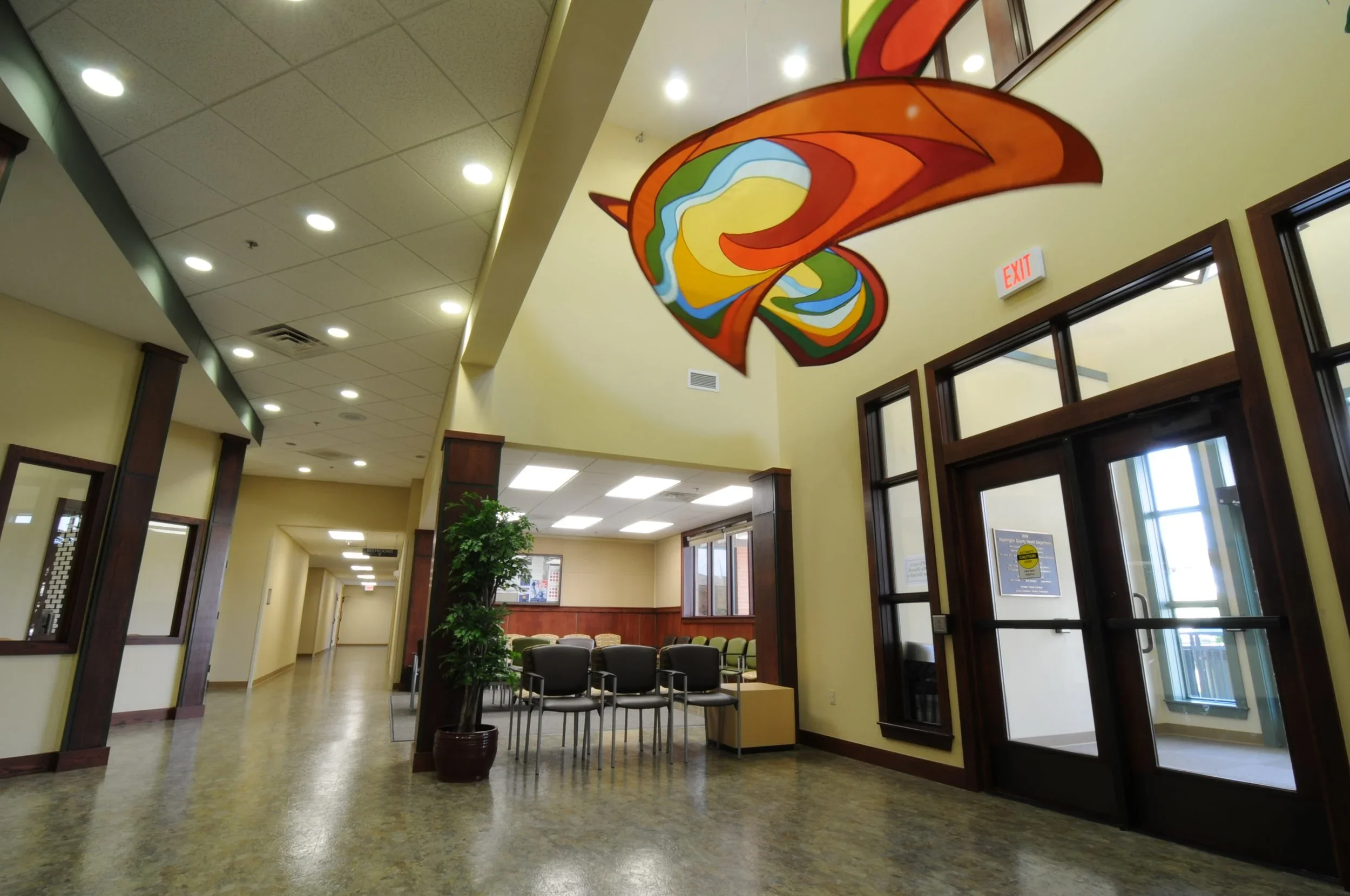 Interior of a waiting room with a large, colorful abstract hanging sculpture and row of chairs.