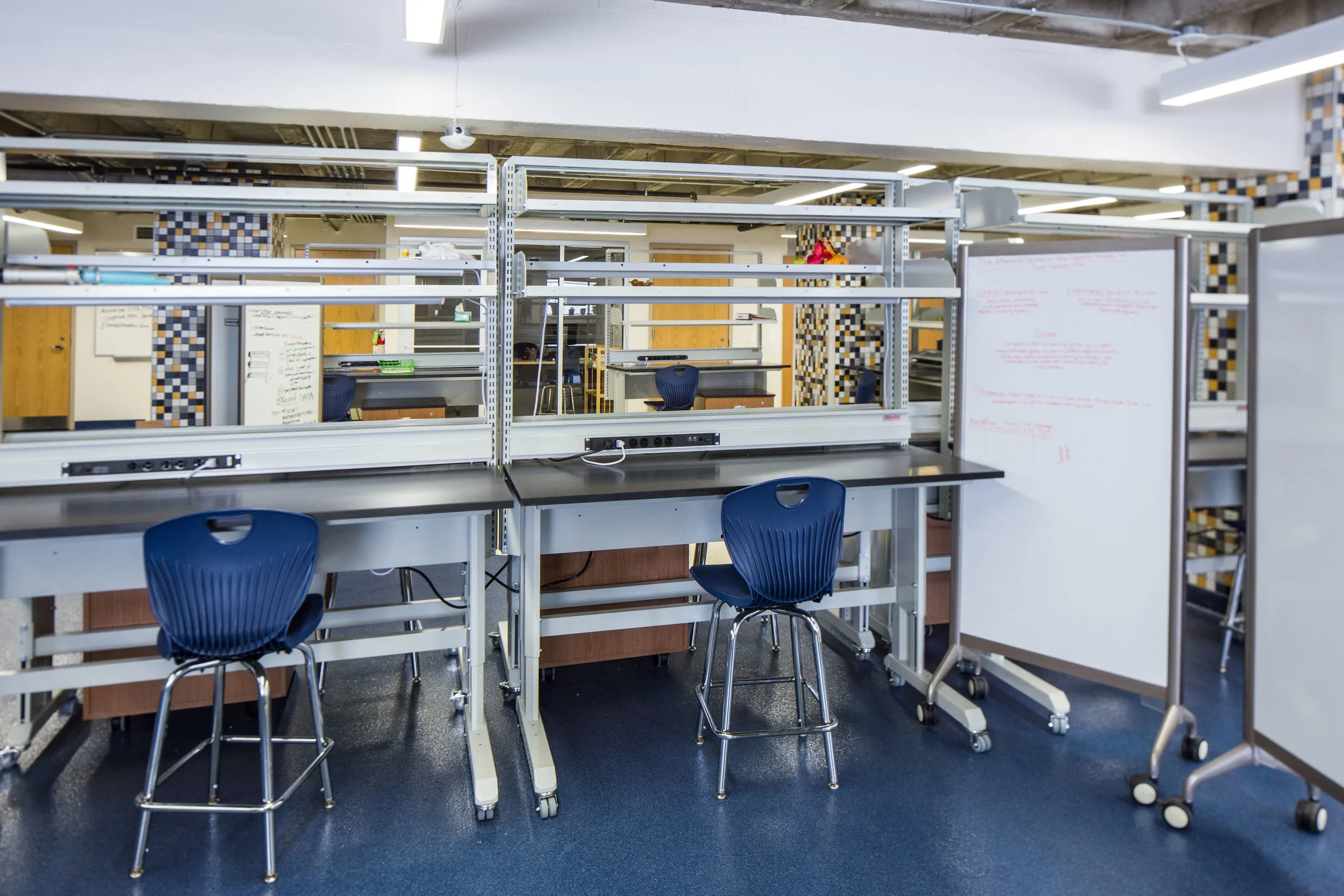 Empty classroom with desks, chairs, whiteboard, and white electrical cords on black desks in a school or office setting.