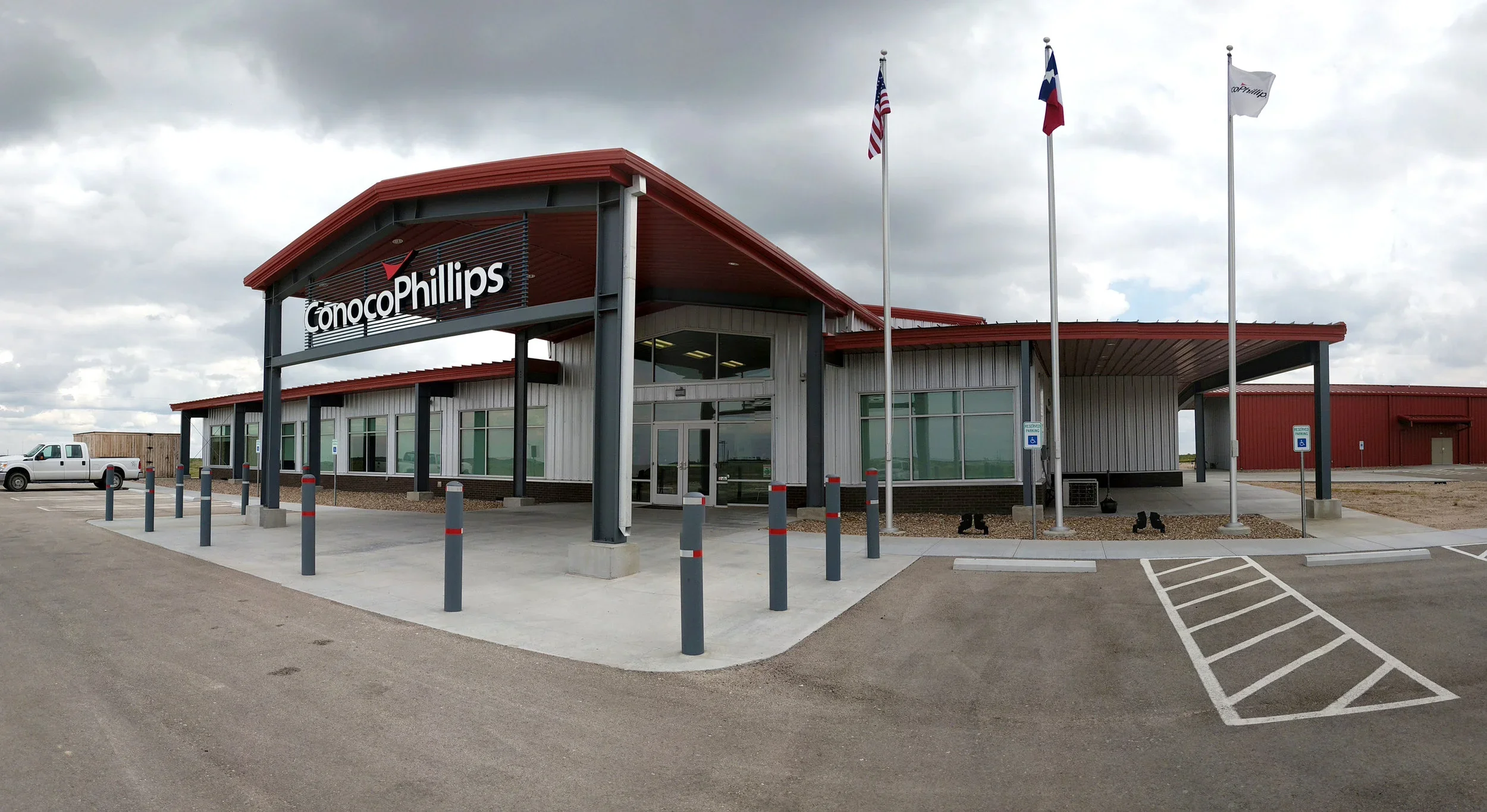 ConocoPhillips building with a large sign, three flags in front, angled parking spaces, and an overcast sky.