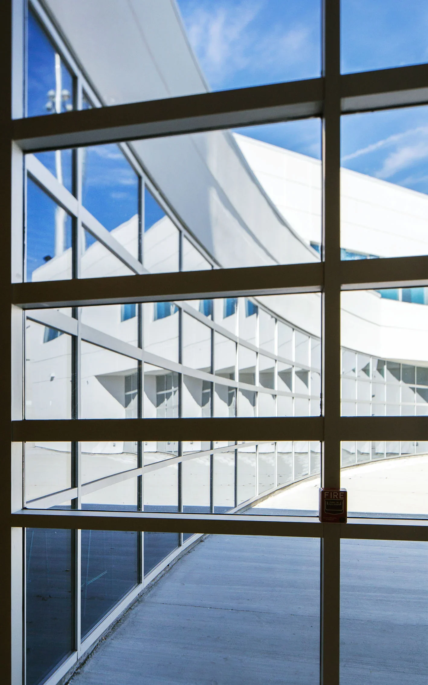 View of modern building with curved white exterior seen through a large grid window, with a blue sky in the background.